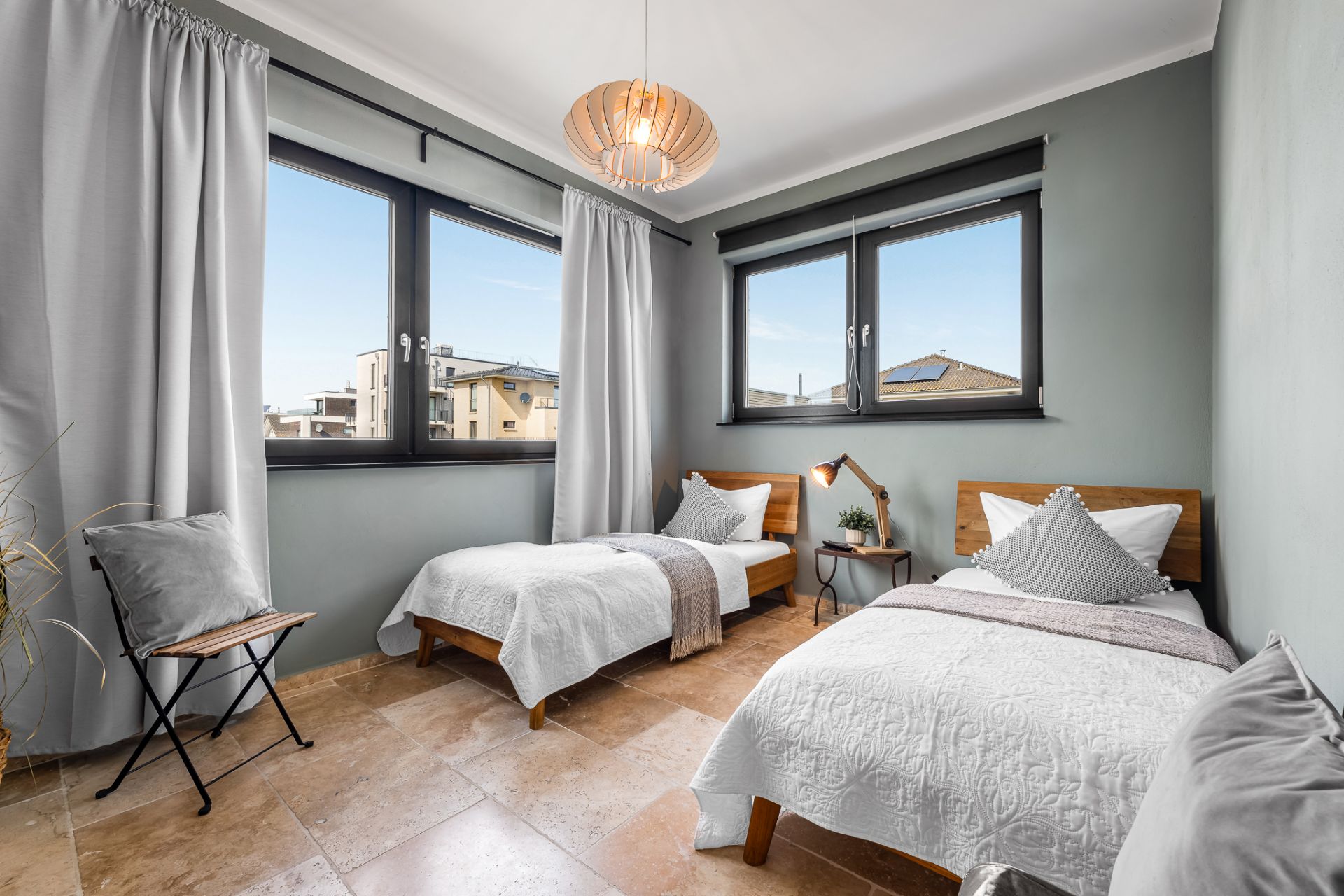 Helles Schlafzimmer mit zwei Einzelbetten, großen Fenstern und hellen Vorhängen.