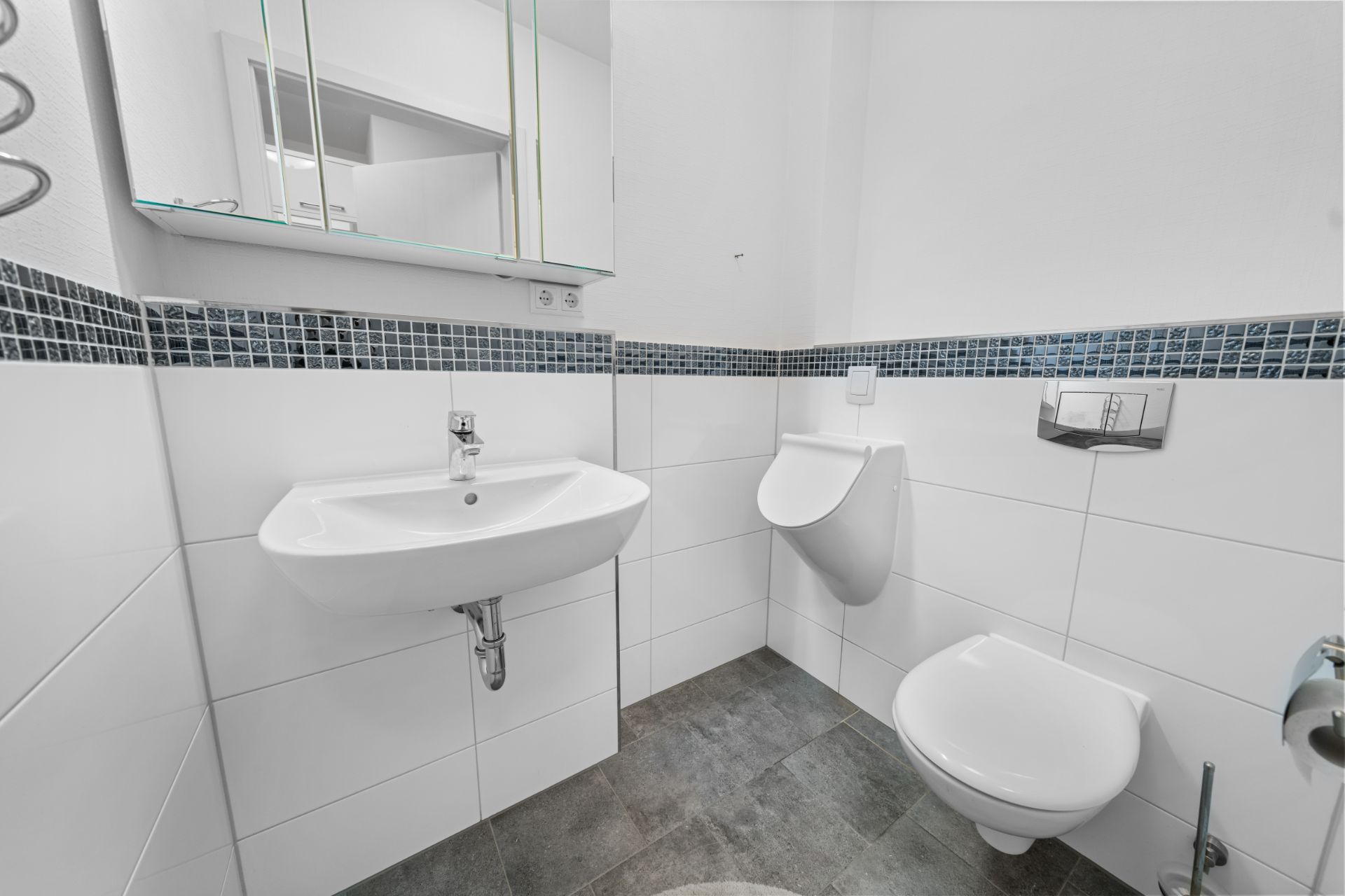 Modernes Badezimmer mit Waschbecken, Urinal, Toilette und Spiegel an der Wand.