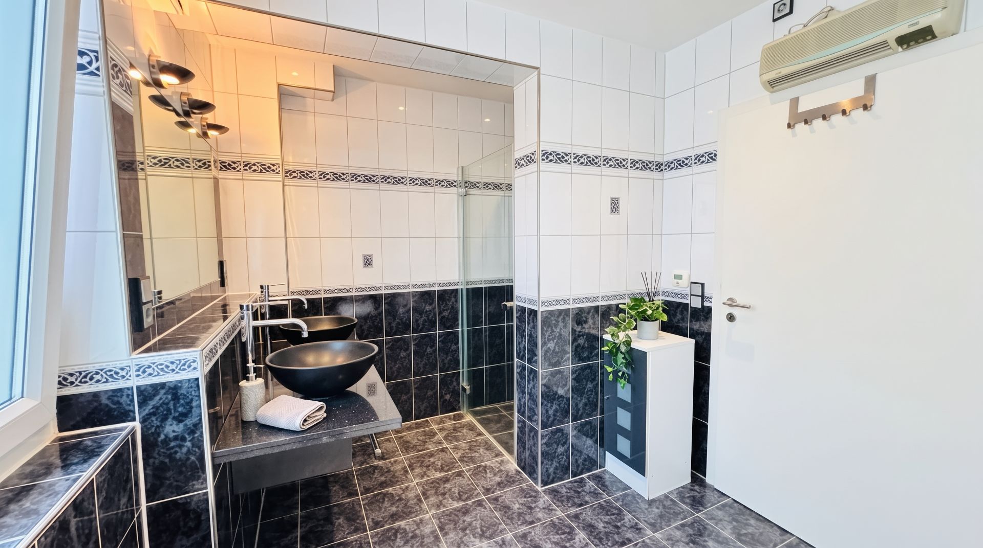Modernes Badezimmer mit zwei schwarzen Waschbecken, großer Spiegelwand und begehbarer Dusche.
