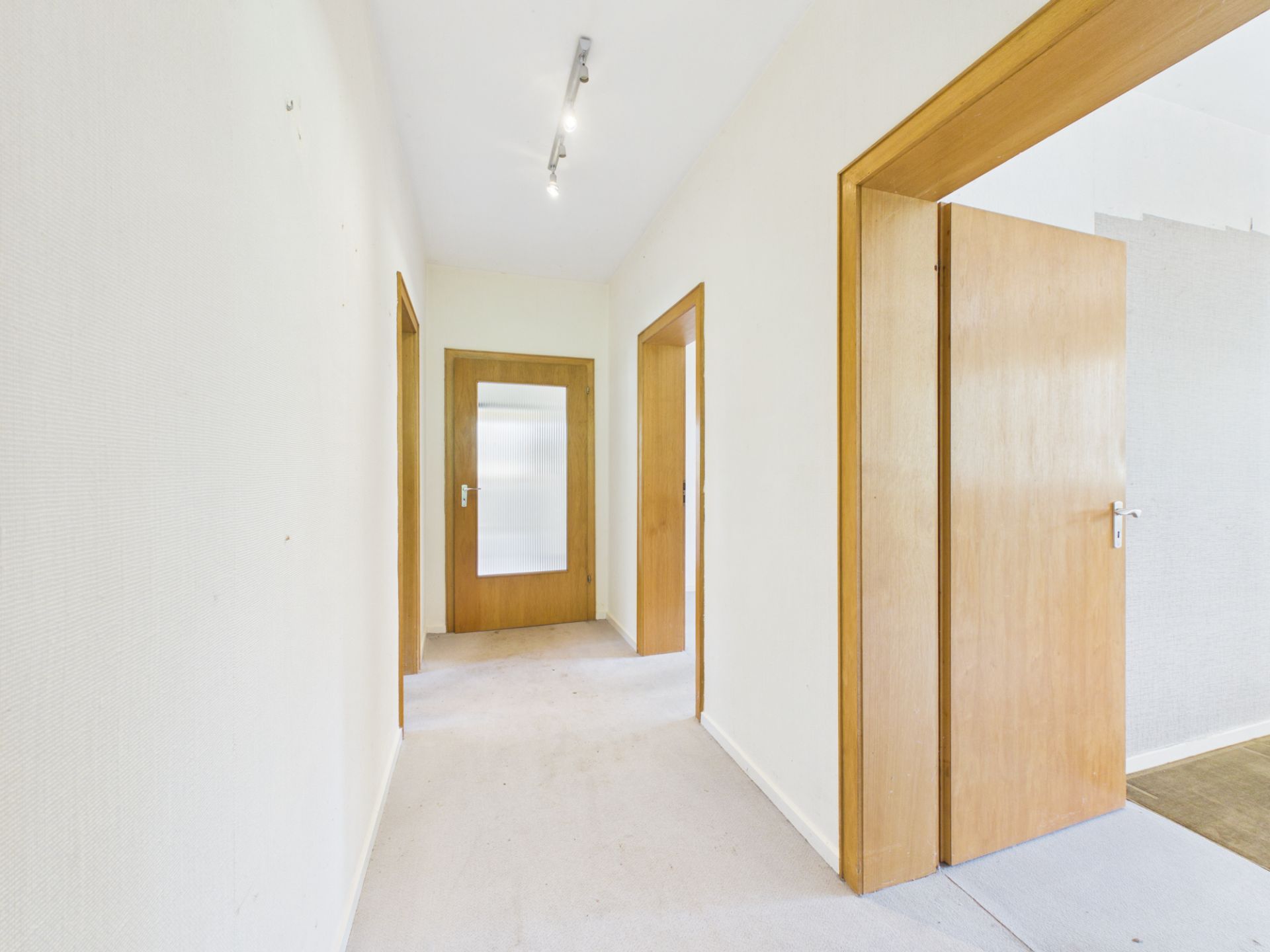 Heller Flur mit hellen Wänden und mehreren Holztüren in einer Wohnung.