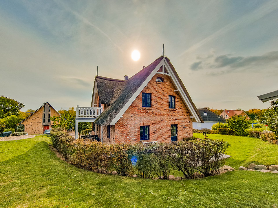 Backsteinhaus mit Reetdach in einem gepflegten Garten bei Sonnenschein.