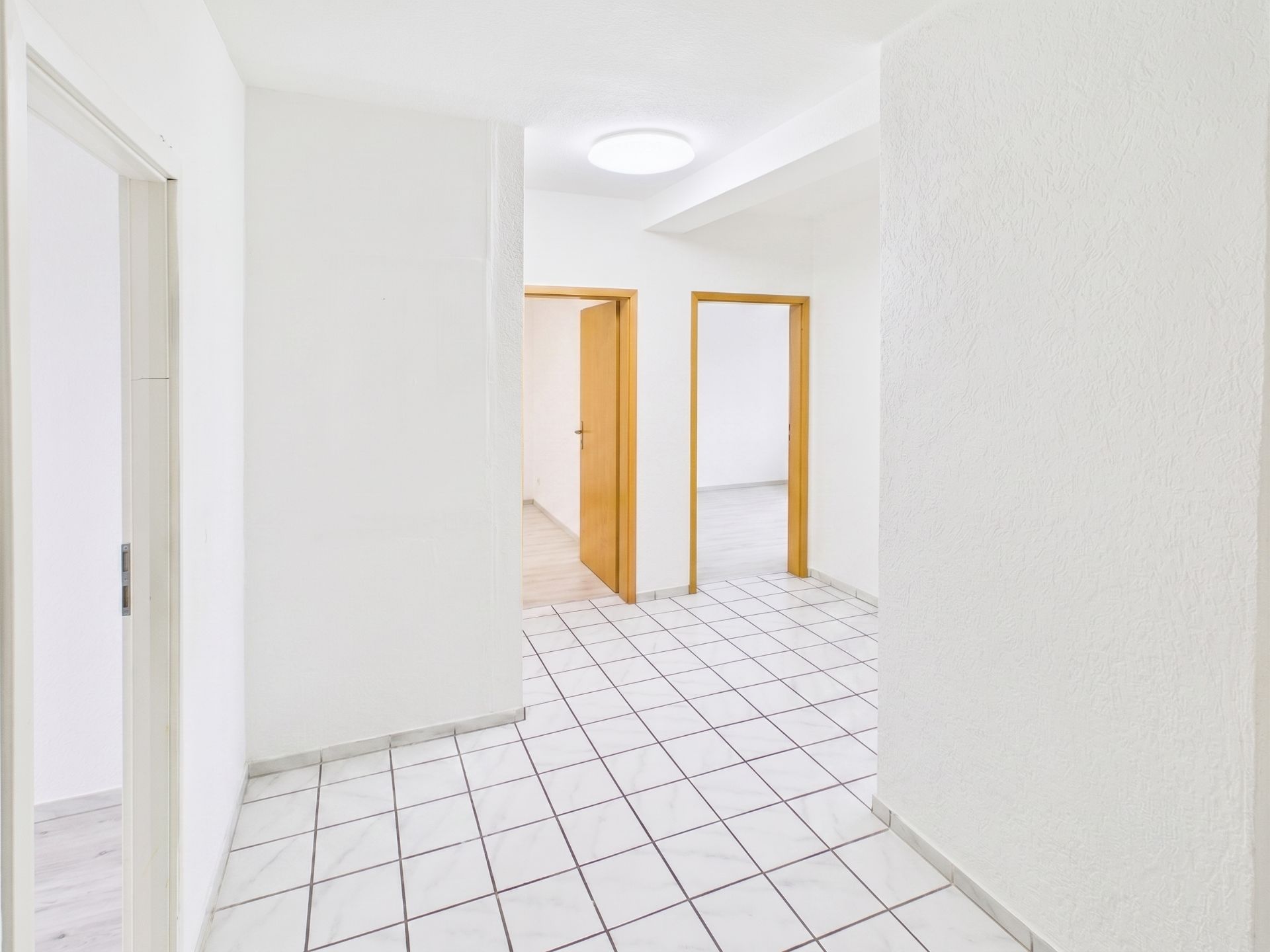 Heller Flur mit weißen Wänden, Fliesenboden und mehreren Holztüren zu angrenzenden Räumen.