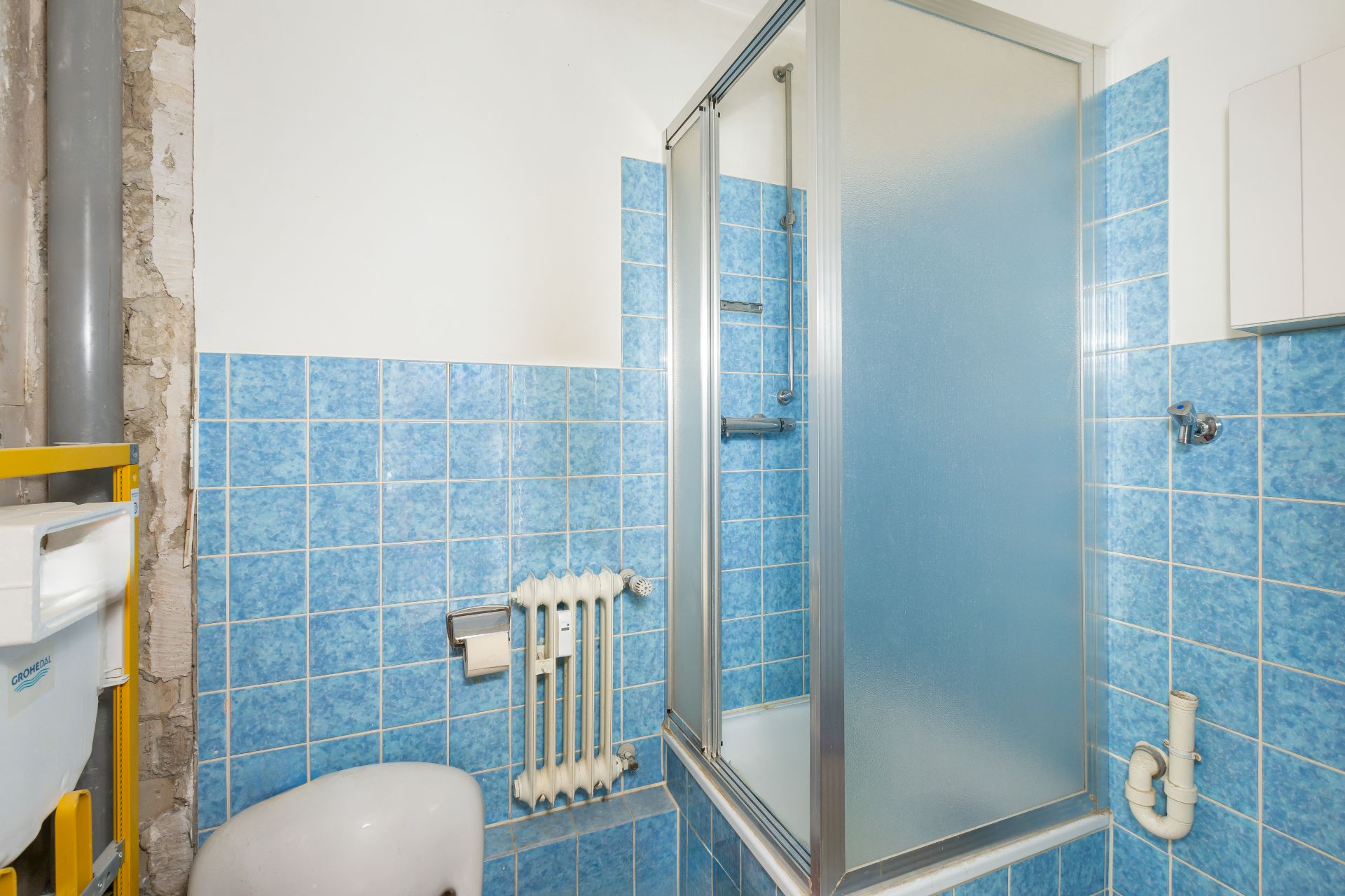 Kleines Badezimmer mit blauen Fliesen, Dusche mit Glaswand und sichtbarer Heizung.