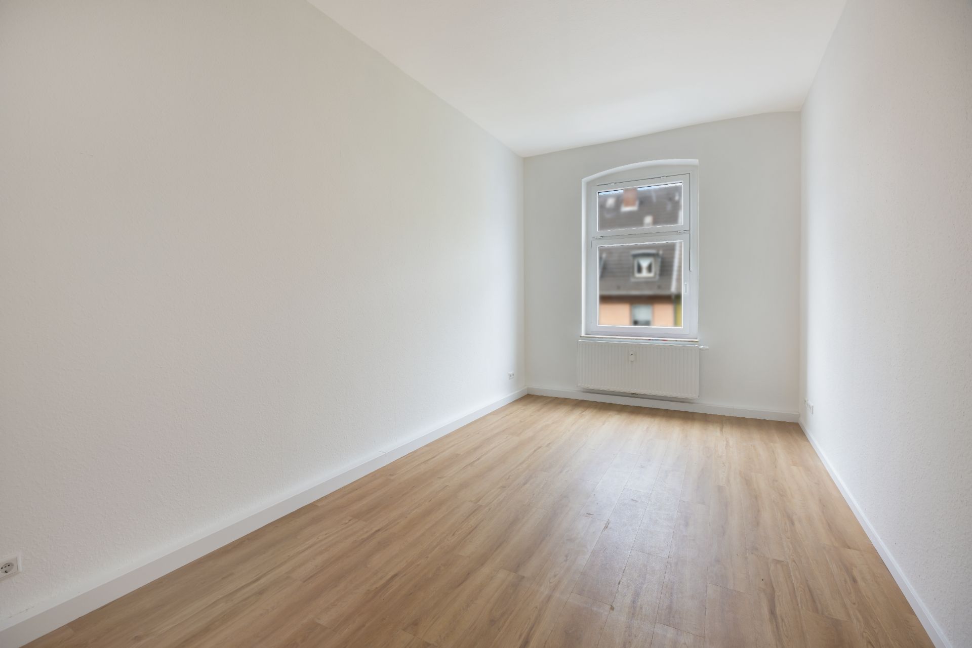 Leerer Raum mit Holzfußboden, weißem Fenster und weißen Wänden.