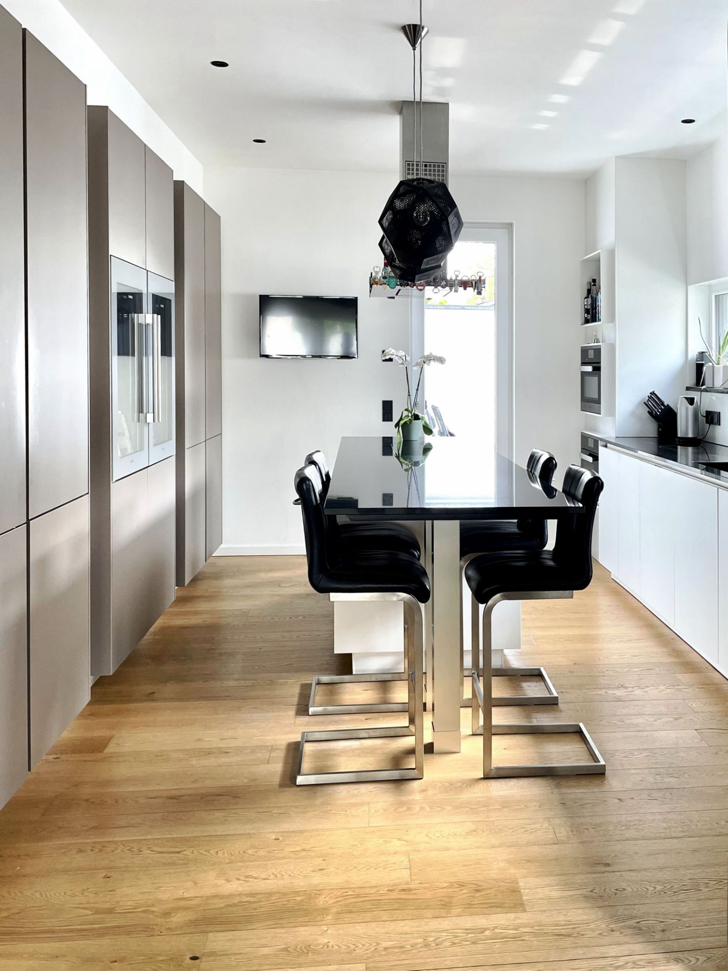 Moderne Küche mit Holzboden, Esstisch, vier Stühlen und Hängelampe, Fernseher an der Wand.