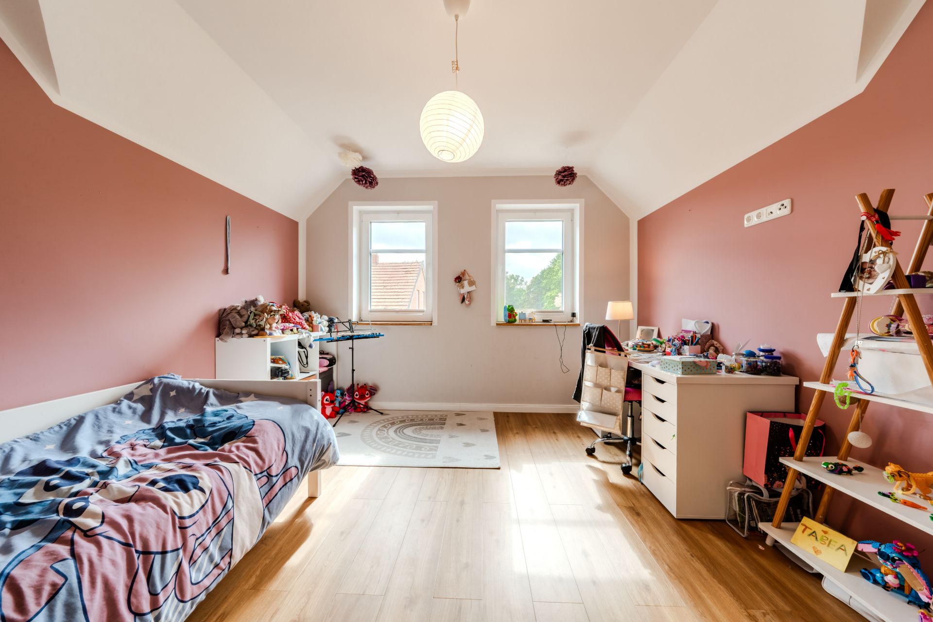 Kinderzimmer mit Einzelbett, zwei Fenstern, Schreibtisch und Spielzeugregal.