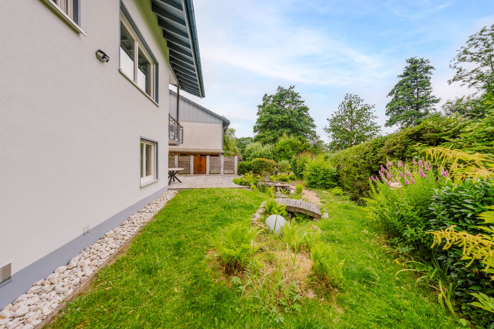 Gepflegter Garten mit Rasen, Büschen und Steinen neben einem modernen Wohnhaus.