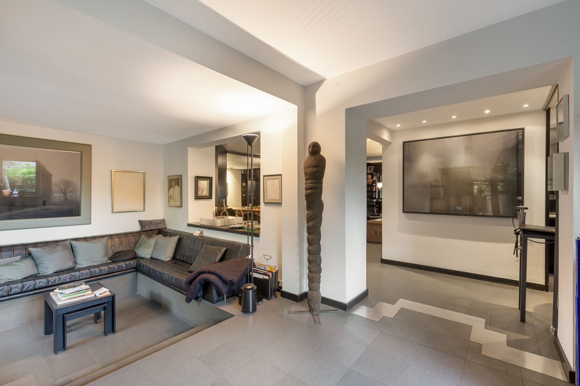Modernes Wohnzimmer mit großer Eckcouch, Kunstwerken an den Wänden und Stehlampe.