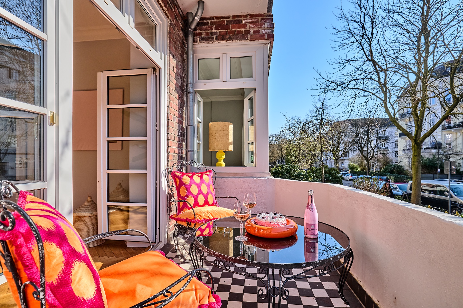 Balkon mit bunten Kissen, Glastisch, Snacks und Blick auf die Straße.
