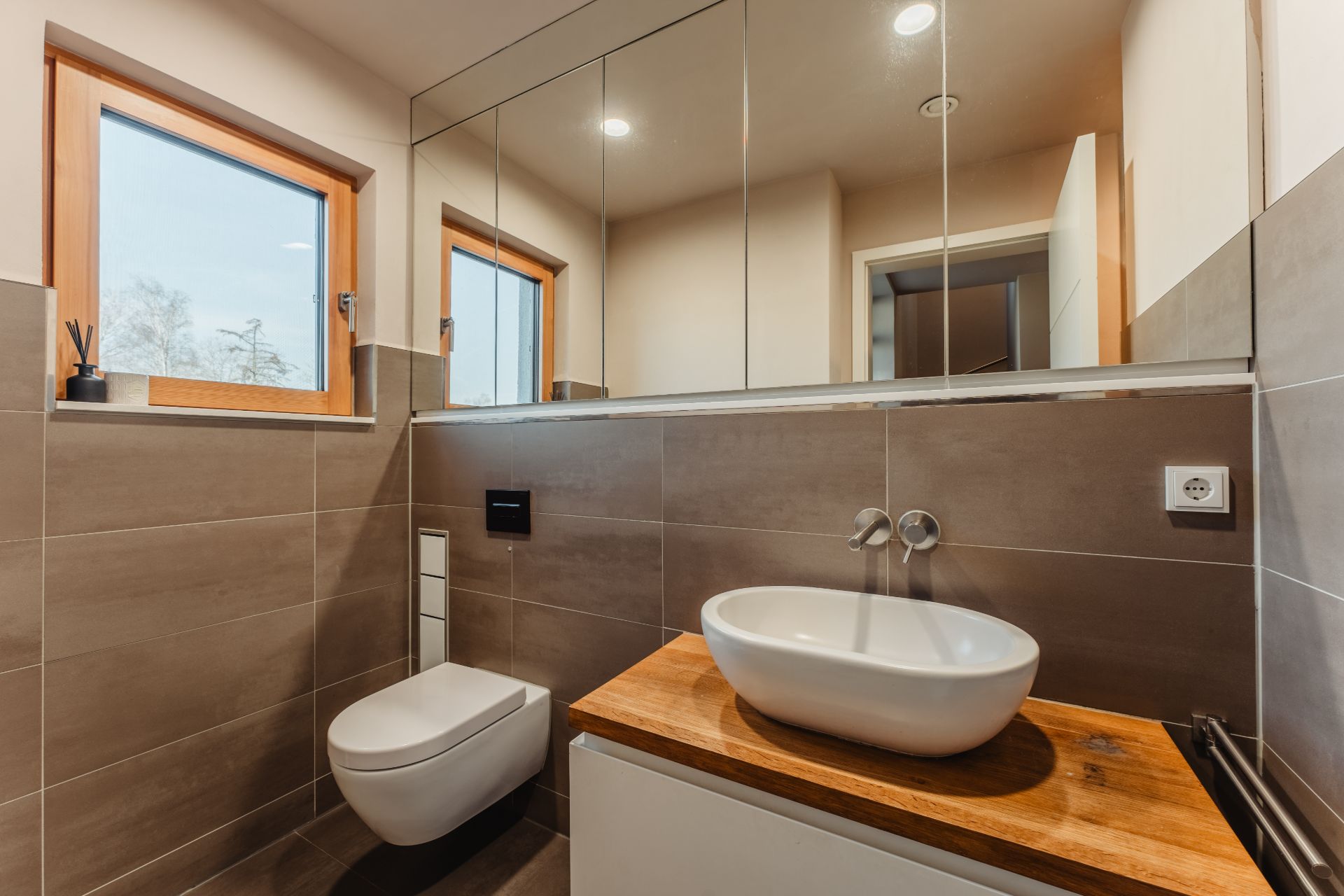 Modernes Bad mit wandhängendem WC, großem Spiegel und Waschbecken auf Holzplatte.