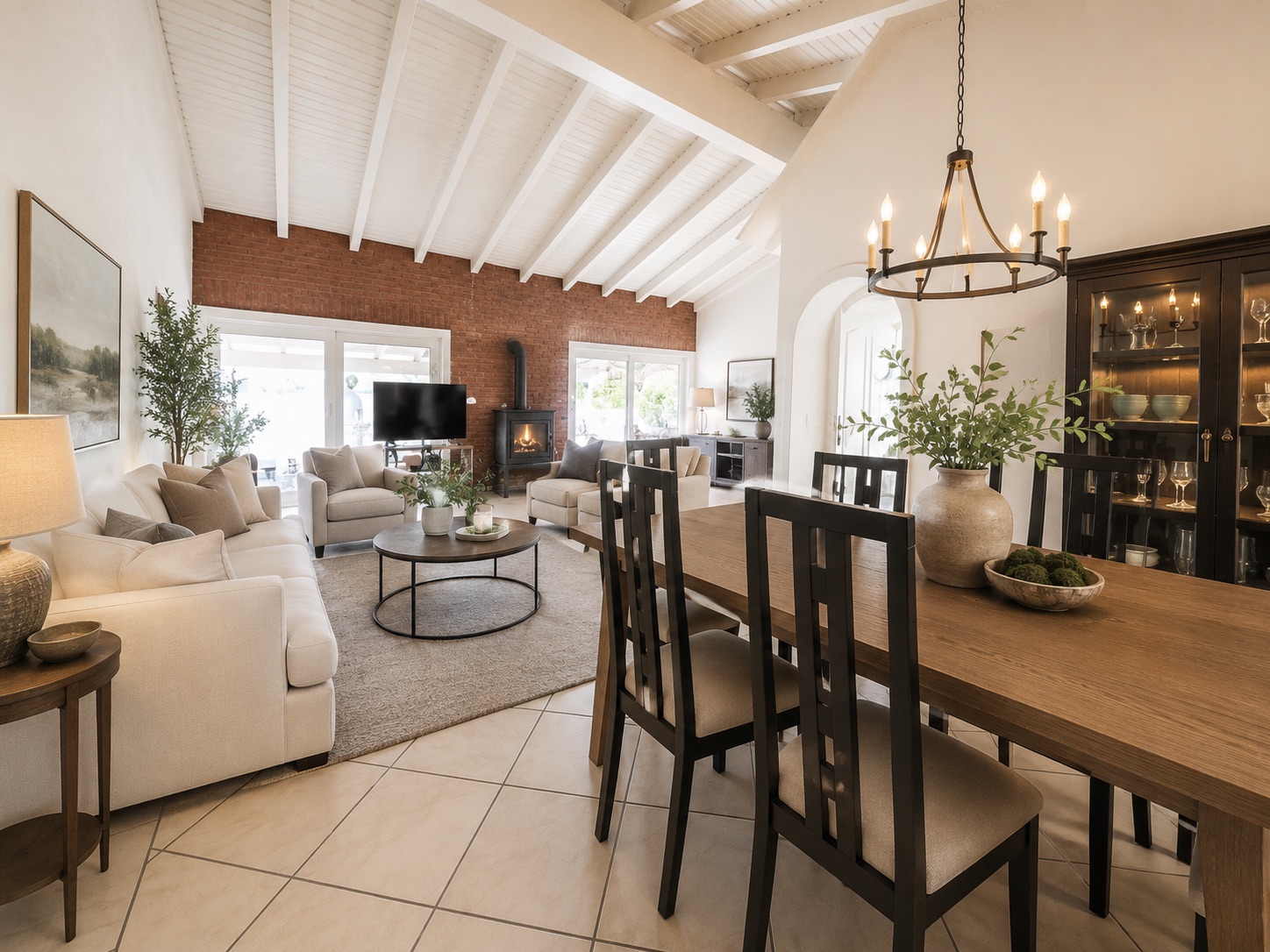 Helles Wohnzimmer mit Holzdecke, Esstisch, Sofa, Kamin und Glastüren.