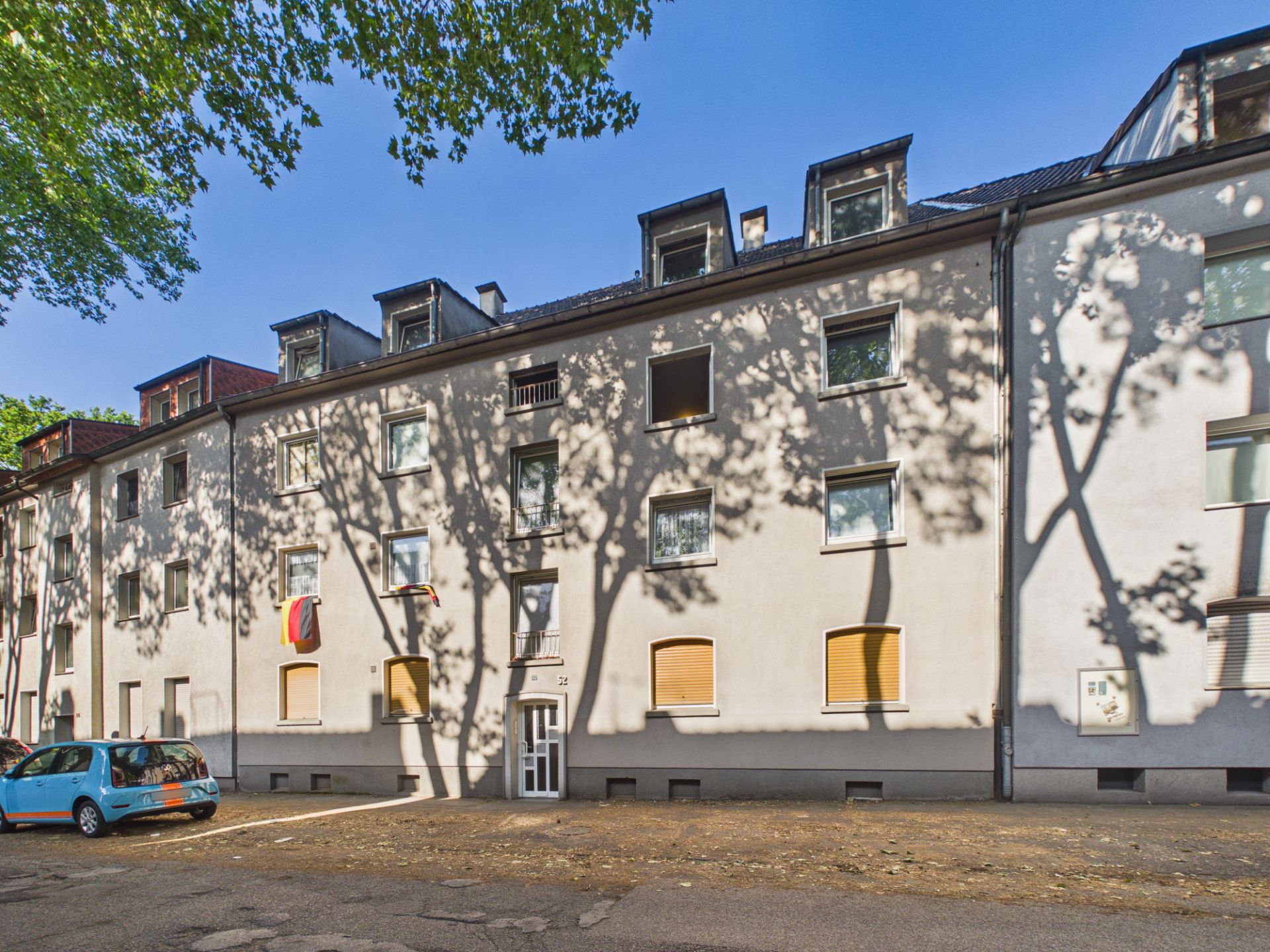 Mehrstöckiges Wohngebäude mit weißen Wänden und mehreren Fenstern, teils mit Rollläden.