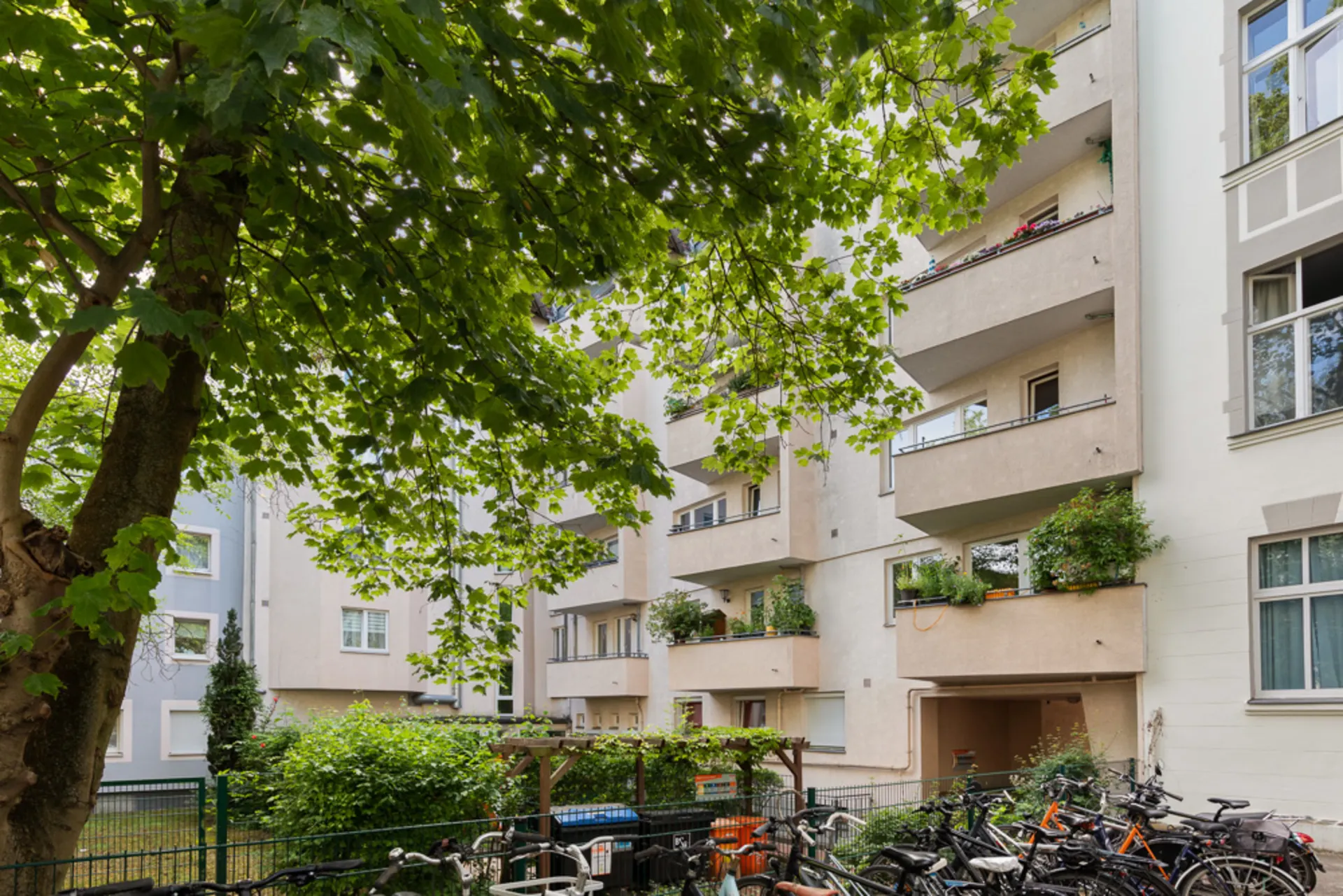 Wohnhaus mit mehreren Balkonen, vielen Pflanzen und Fahrrädern im Vordergrund.