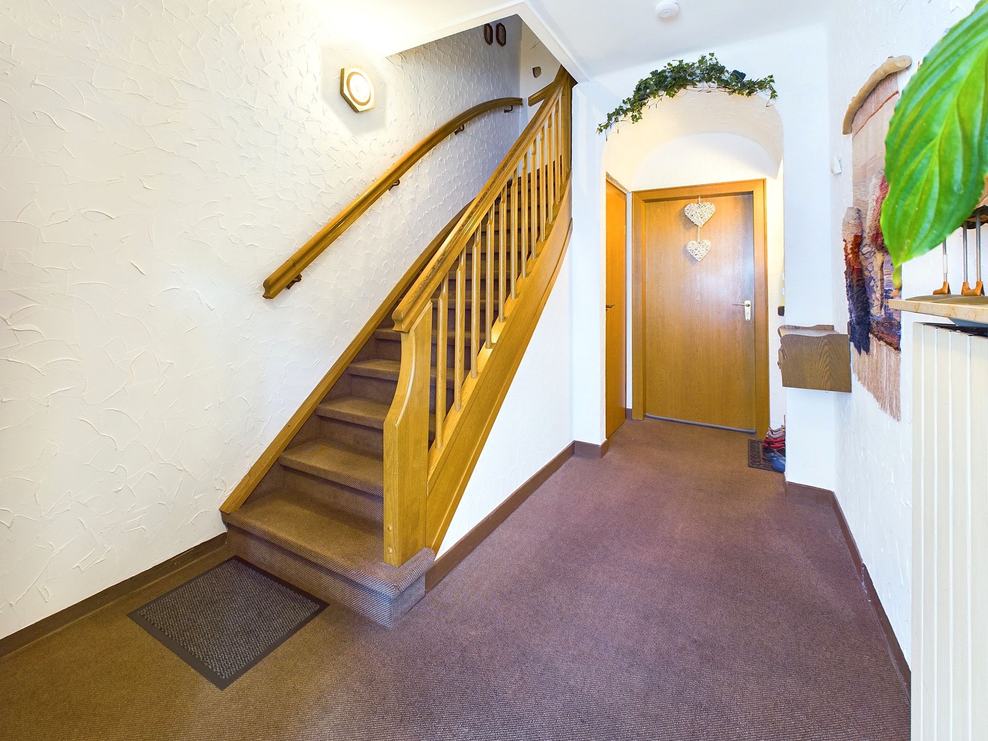 Innenflur mit braunem Teppich, Holztreppe und einer Tür mit Dekoration.