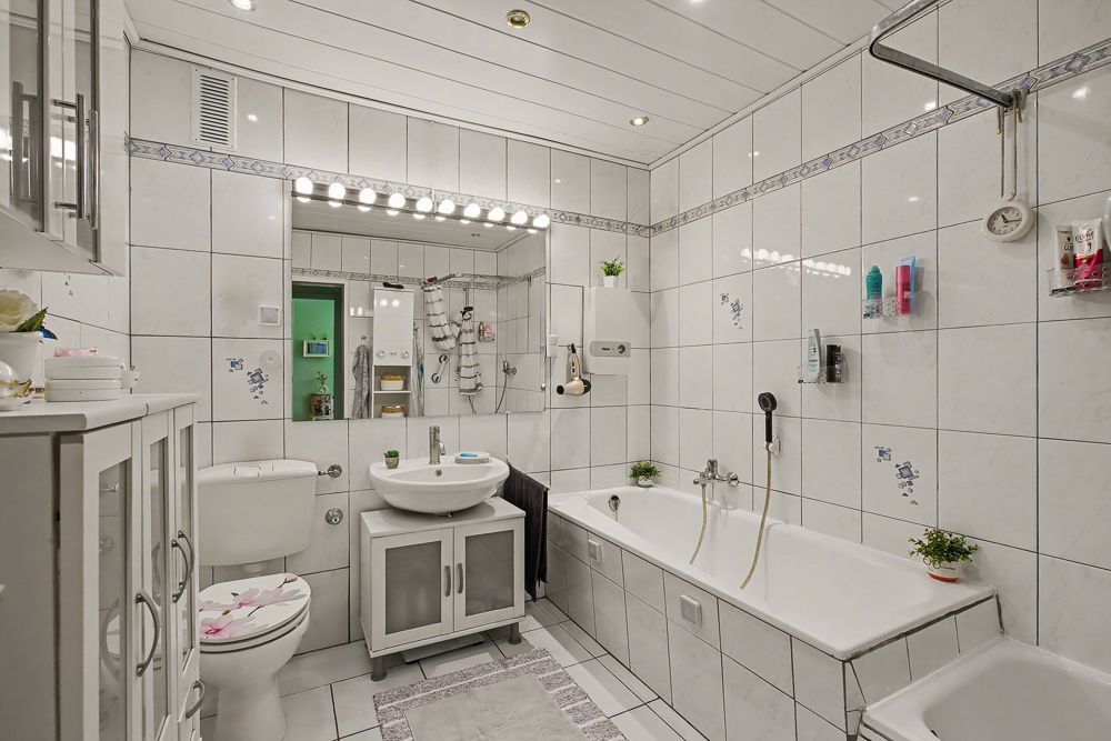 Helles, gefliestes Badezimmer mit Badewanne, Waschbecken, Toilette und großem Spiegel.