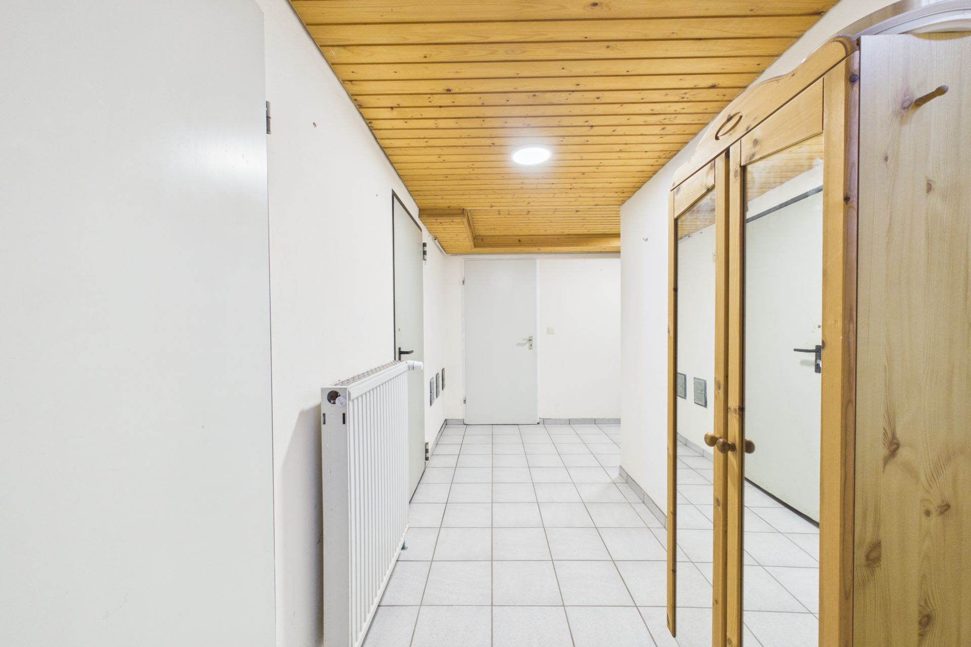 Heller Flur mit weißem Fliesenboden, Holzbalkendecke und Spiegelschrank.