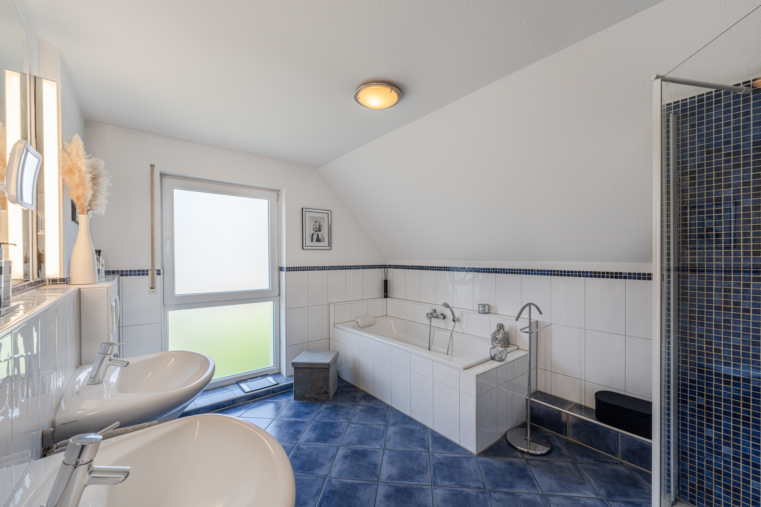 Modernes Badezimmer mit Badewanne, Doppelwaschbecken und Dusche, blaue Fliesen und großes Fenster.