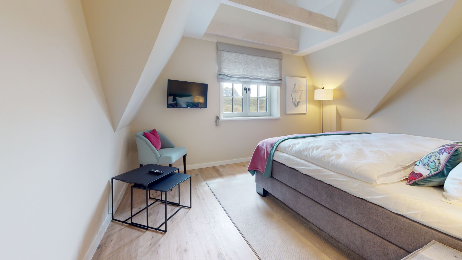 Helles Schlafzimmer mit Doppelbett, Sessel, Fernseher, Fenstern und Stehlampe.