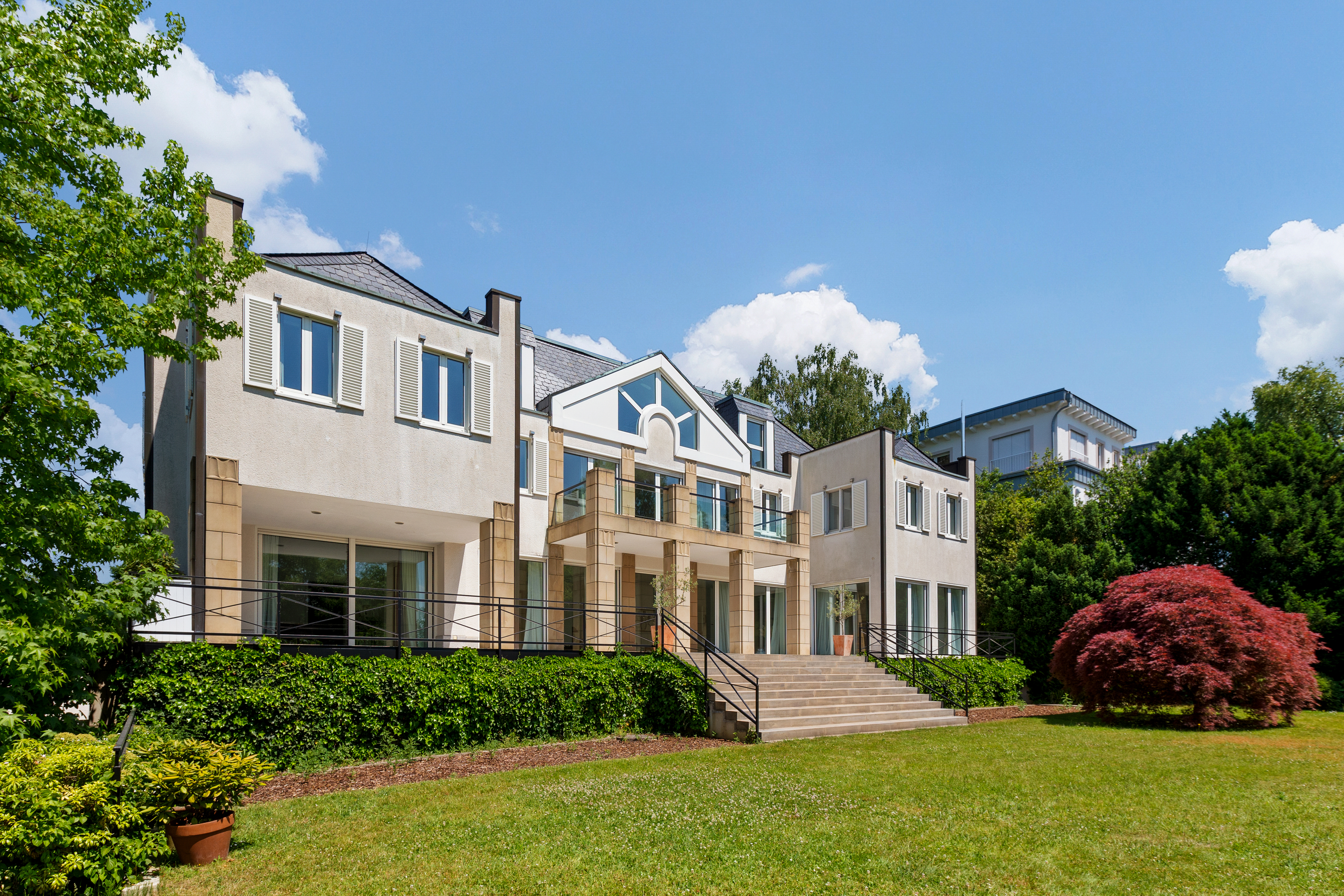 Modernes Wohnhaus mit großen Fenstern, breiter Treppe und gepflegtem Garten.