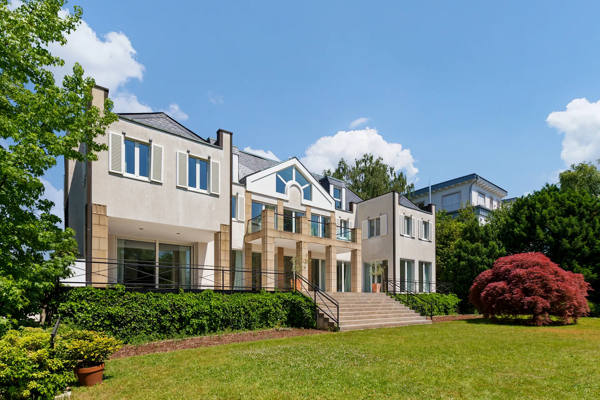 Modernes Wohnhaus mit großen Fenstern, breiter Treppe und gepflegtem Garten.