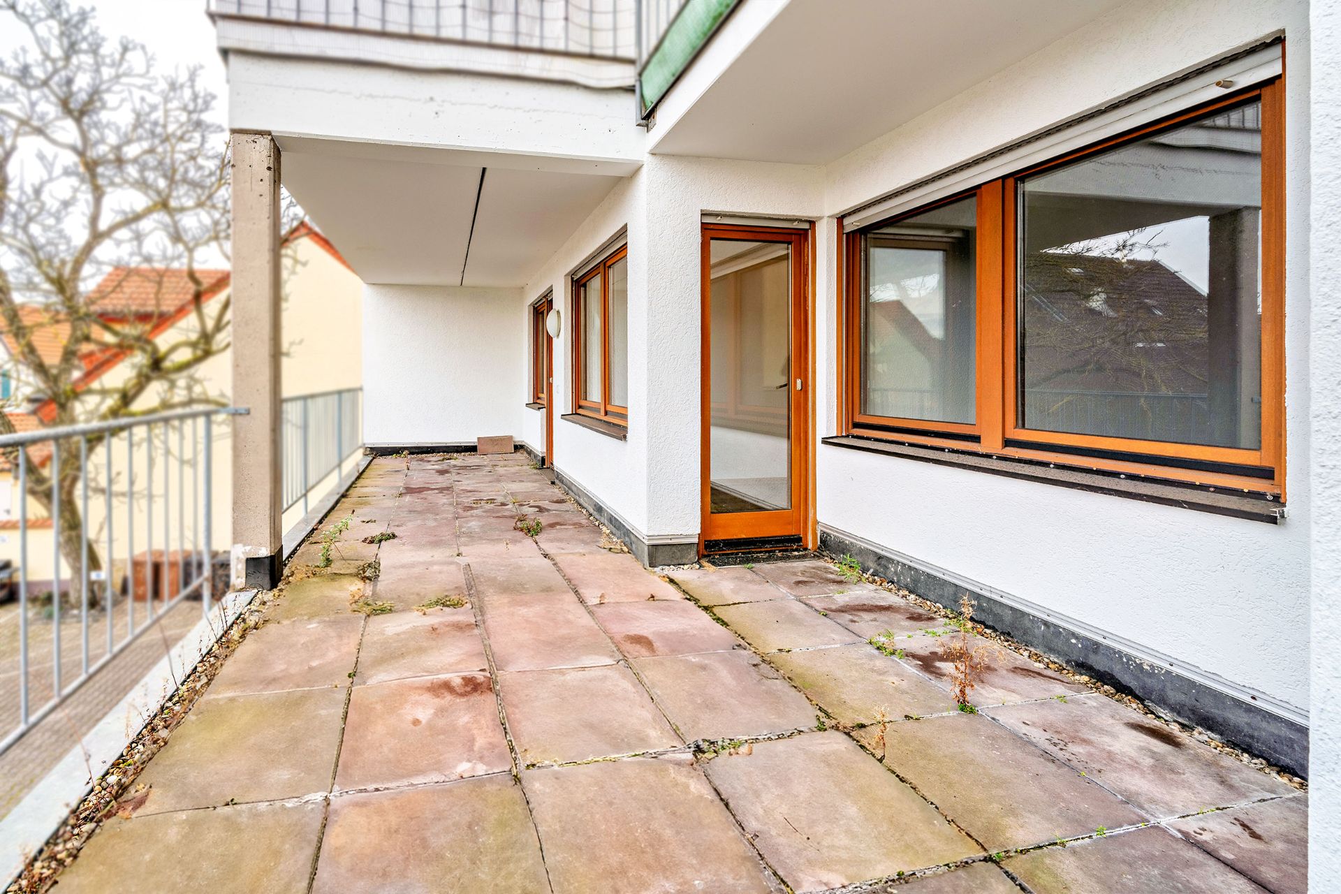 Große Terrasse mit Steinplatten und bodentiefen Fenstern an einem Wohnhaus.