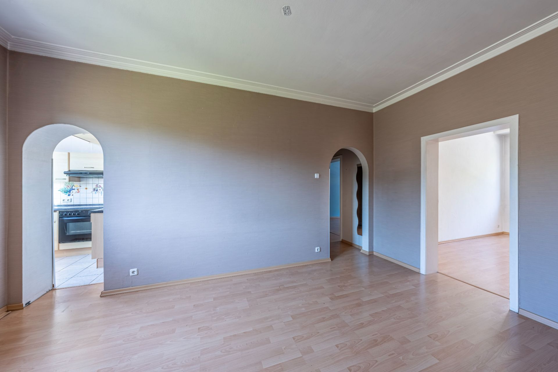 Wohnzimmer mit Holzfußboden, drei Durchgängen und Blick in die Küche.