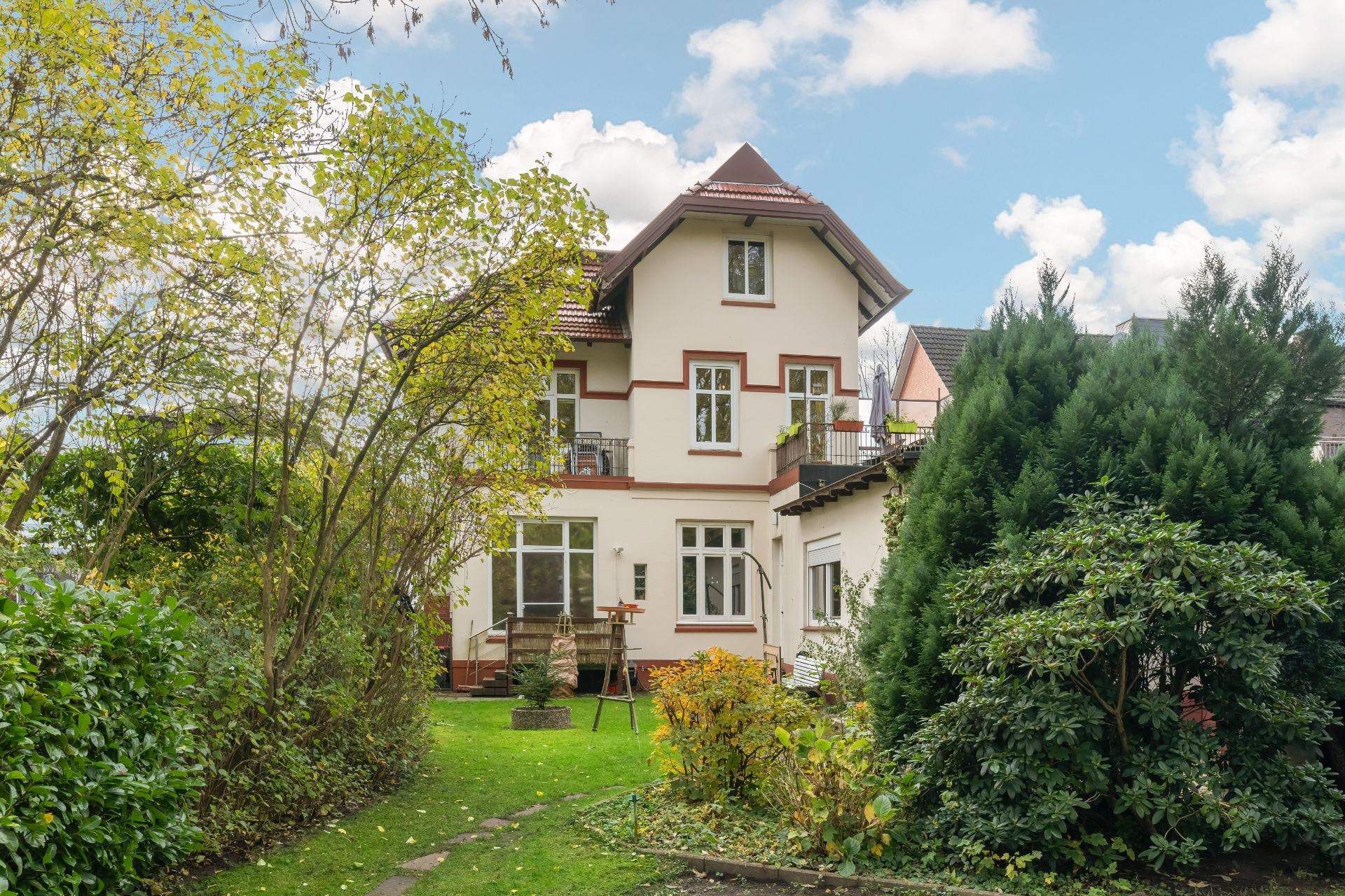 Mehrstöckiges Wohnhaus mit Garten, umgeben von Bäumen und Sträuchern.