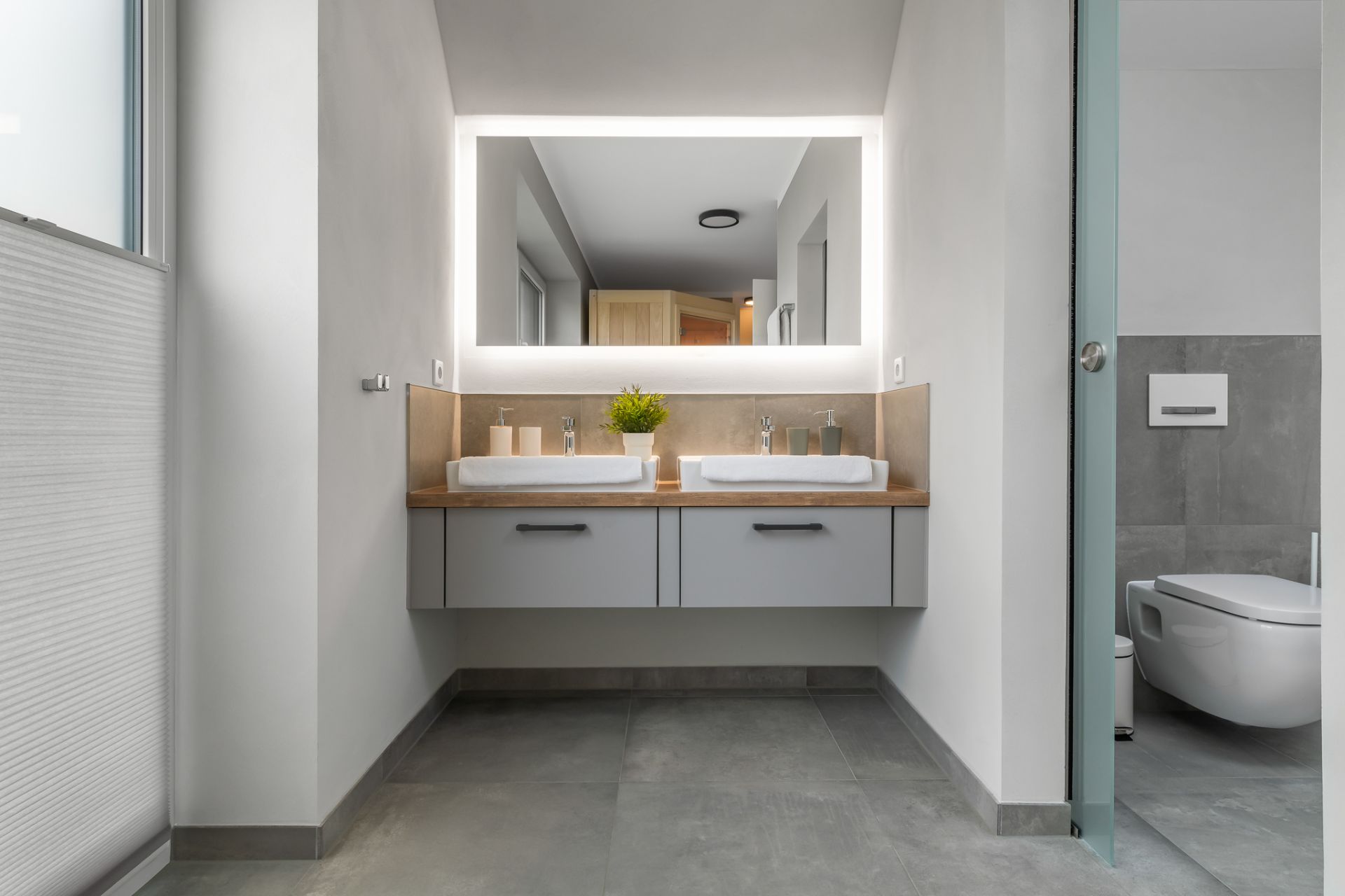 Modernes Badezimmer mit zwei Waschbecken, großem Spiegel und sichtbarer Toilette rechts.