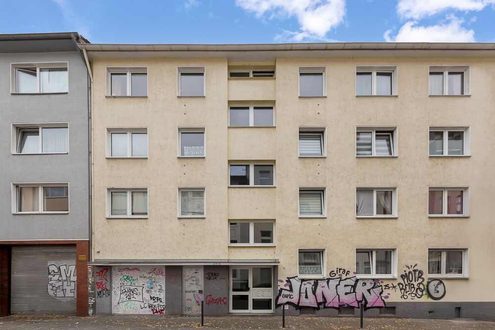 Mehrstöckiges Wohnhaus mit mehreren Fenstern und Graffiti an der Fassade.