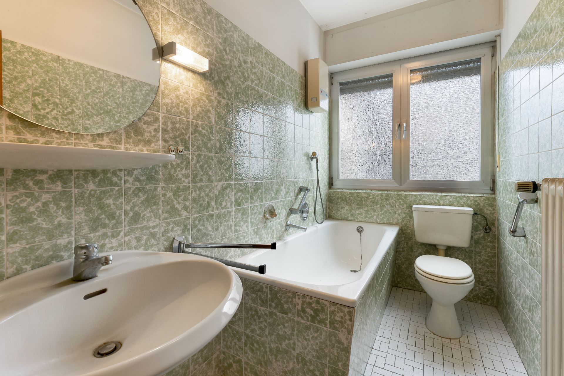Badezimmer mit Badewanne, Waschbecken, Toilette und Fenster, grüne Fliesen an den Wänden.