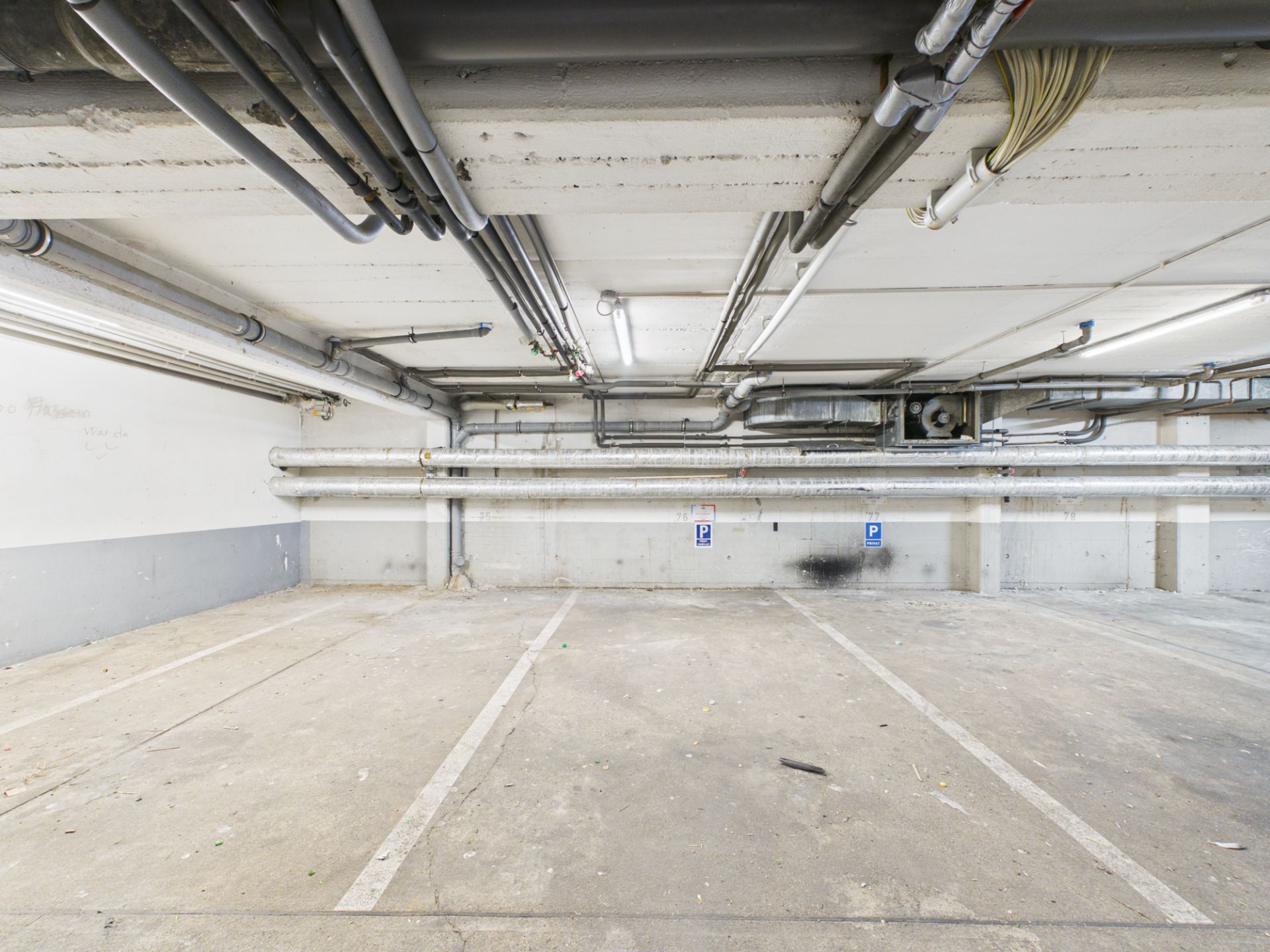 Leerer Tiefgaragenstellplatz mit markierten Parklinien und sichtbaren Rohren an der Decke.