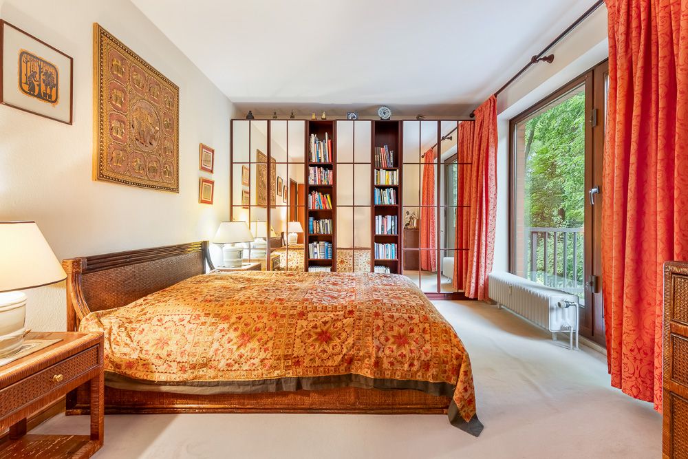 Gemütliches Schlafzimmer mit großem Bett, Bücherregal und Fenster mit roten Vorhängen zum Garten.