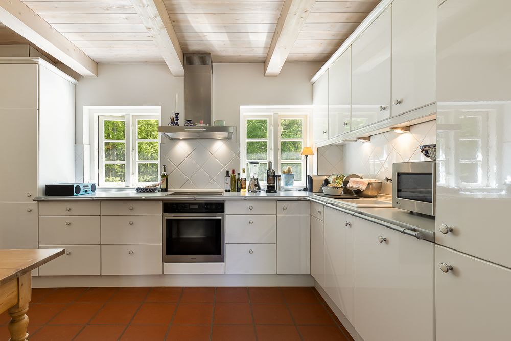 Moderne, helle Einbauküche mit weißen Schränken, Küchengeräten und Tageslicht durch Fenster.
