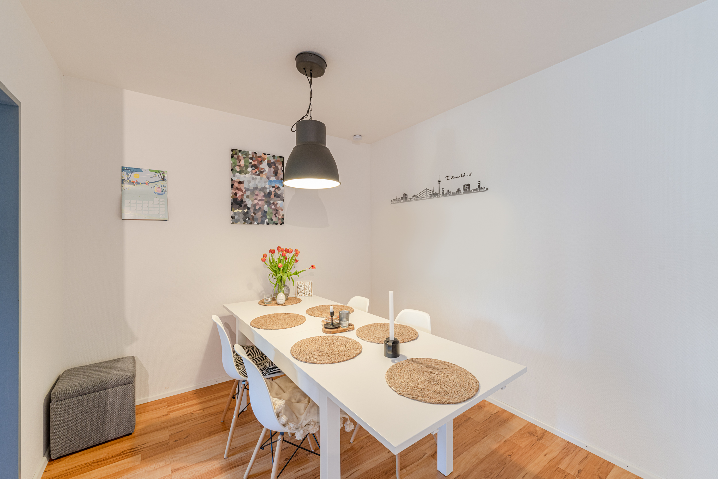 Essbereich mit weißem Tisch, vier Stühlen, Hängelampe und Vase mit Tulpen.