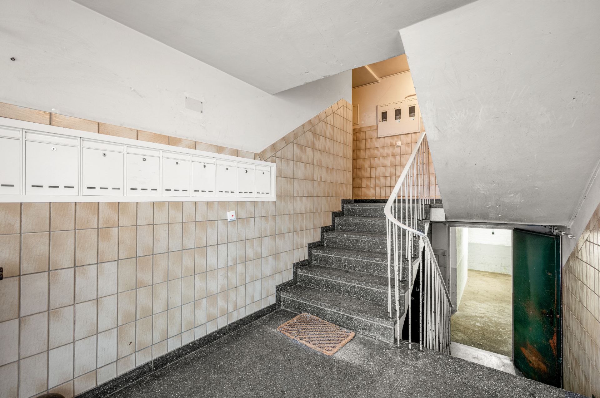 Treppenhaus mit Briefkästen an der Wand und gefliesten Wänden, Zugang zu zwei Etagen.
