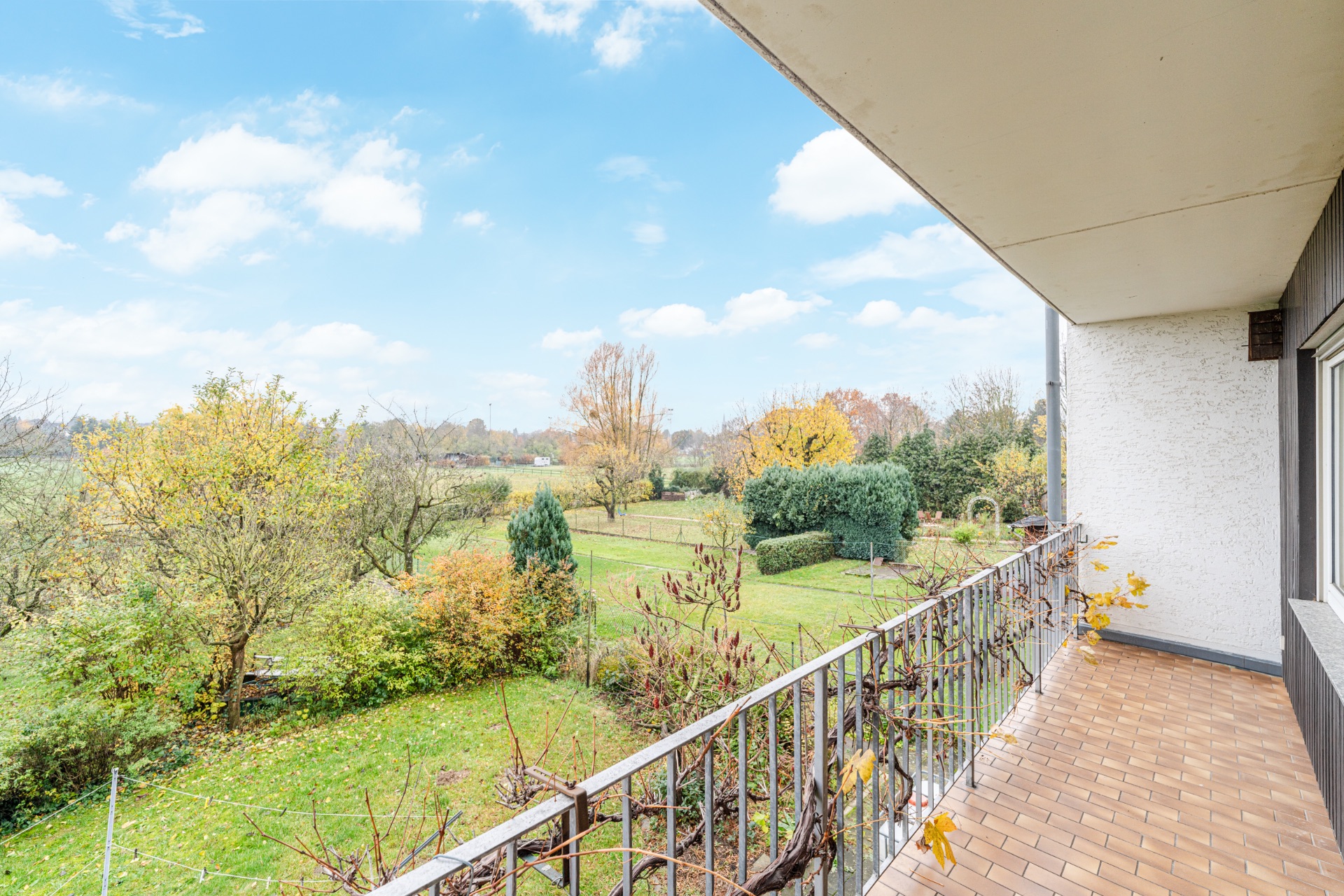 Balkon mit Blick auf einen grünen Garten mit Bäumen und Sträuchern bei klarem Himmel.