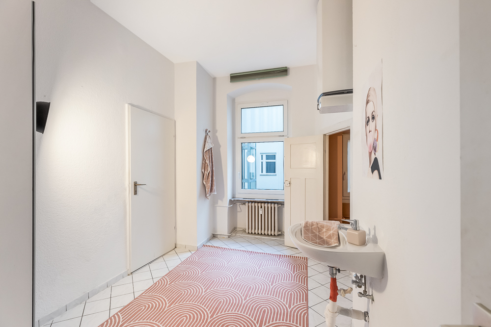 Heller Flur mit Fenster, Waschtisch, Teppich und Wandbild in einer Wohnung.