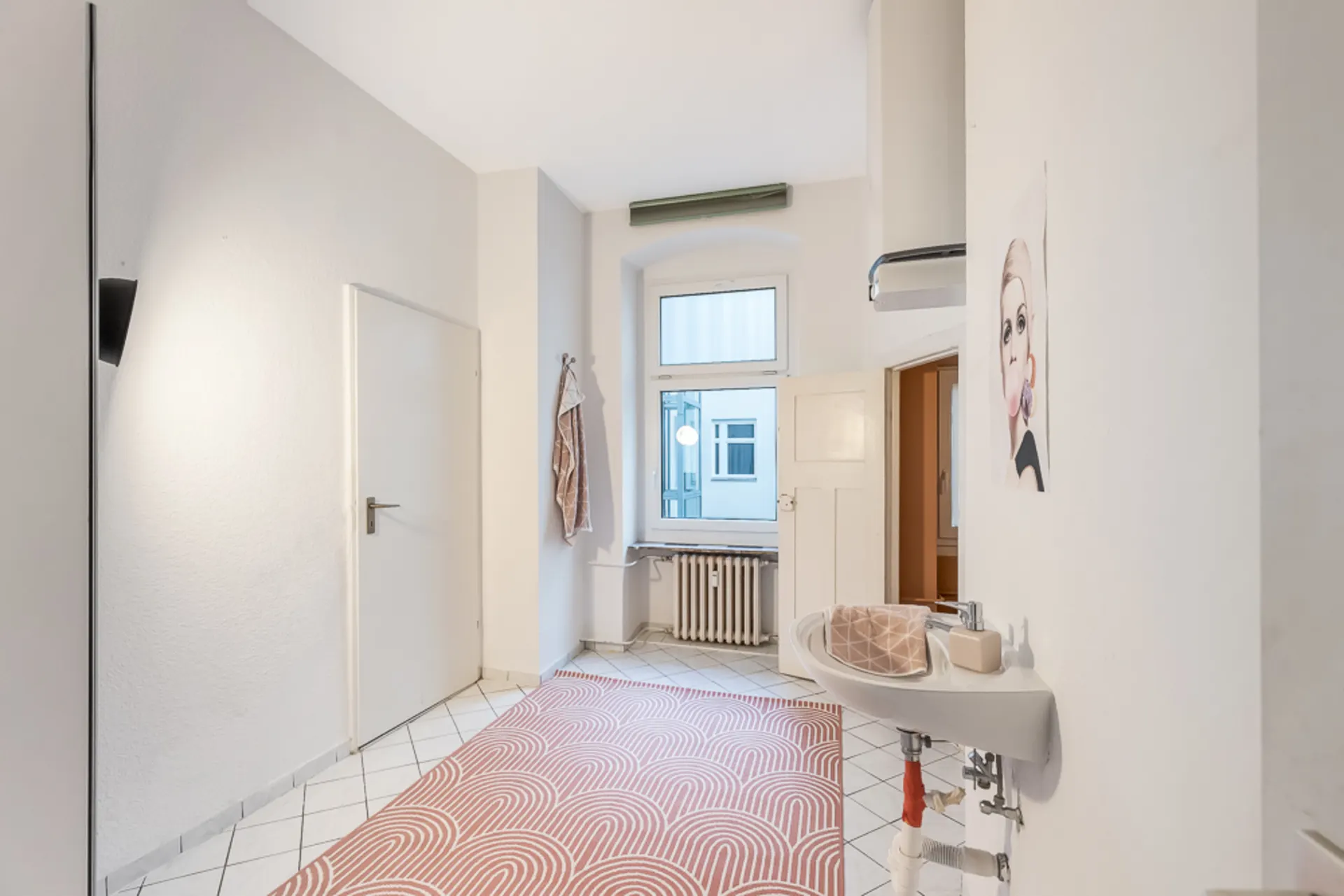 Heller Flur mit Fenster, Waschtisch, Teppich und Wandbild in einer Wohnung.