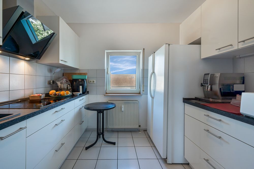 Moderne Küche mit weißen Schränken, großem Kühlschrank, Kaffeemaschine und Fenster mit Ausblick.