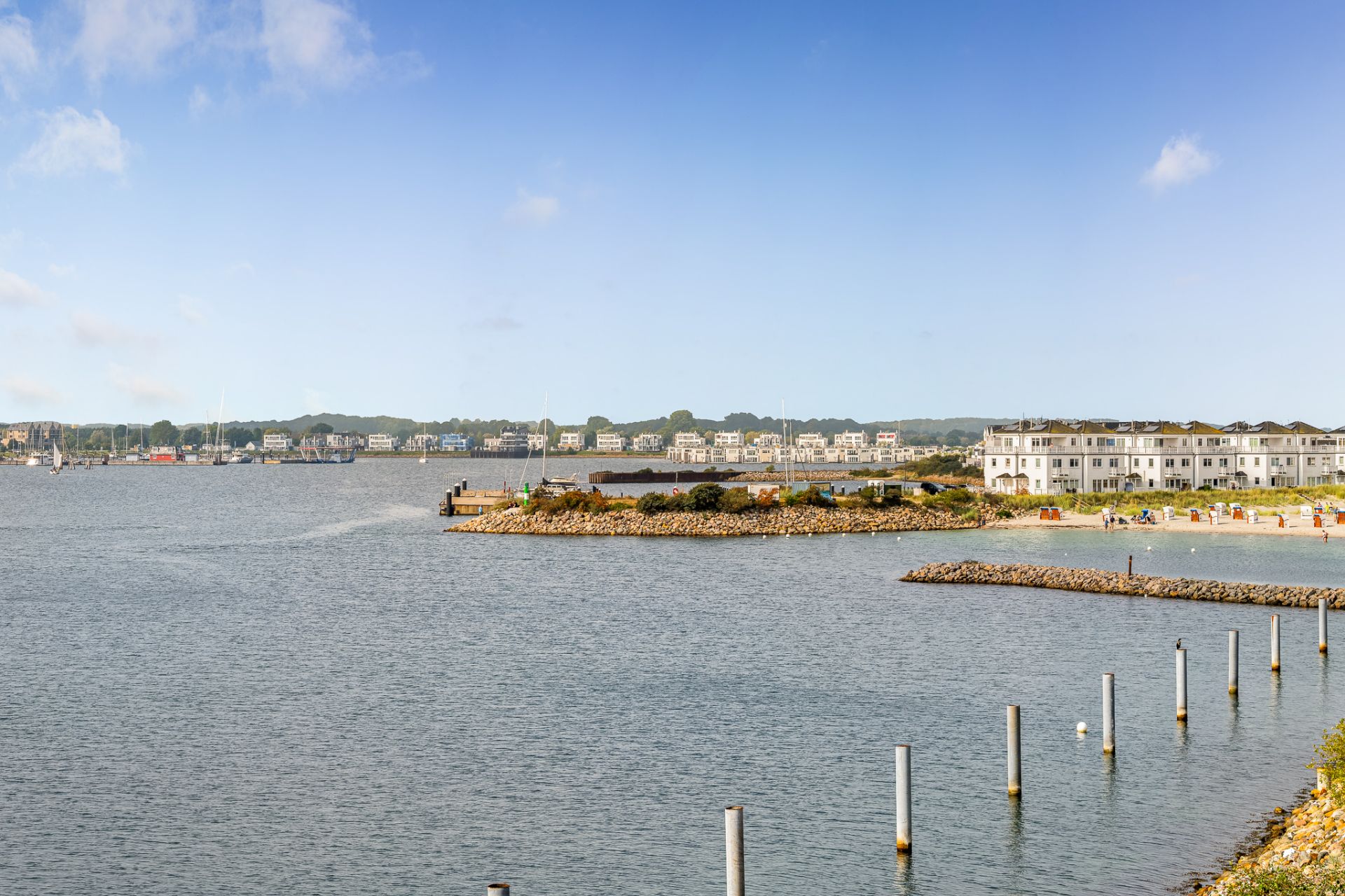 Blick auf das Wasser mit Wohnhäusern und Strand im Hintergrund bei klarem Himmel.
