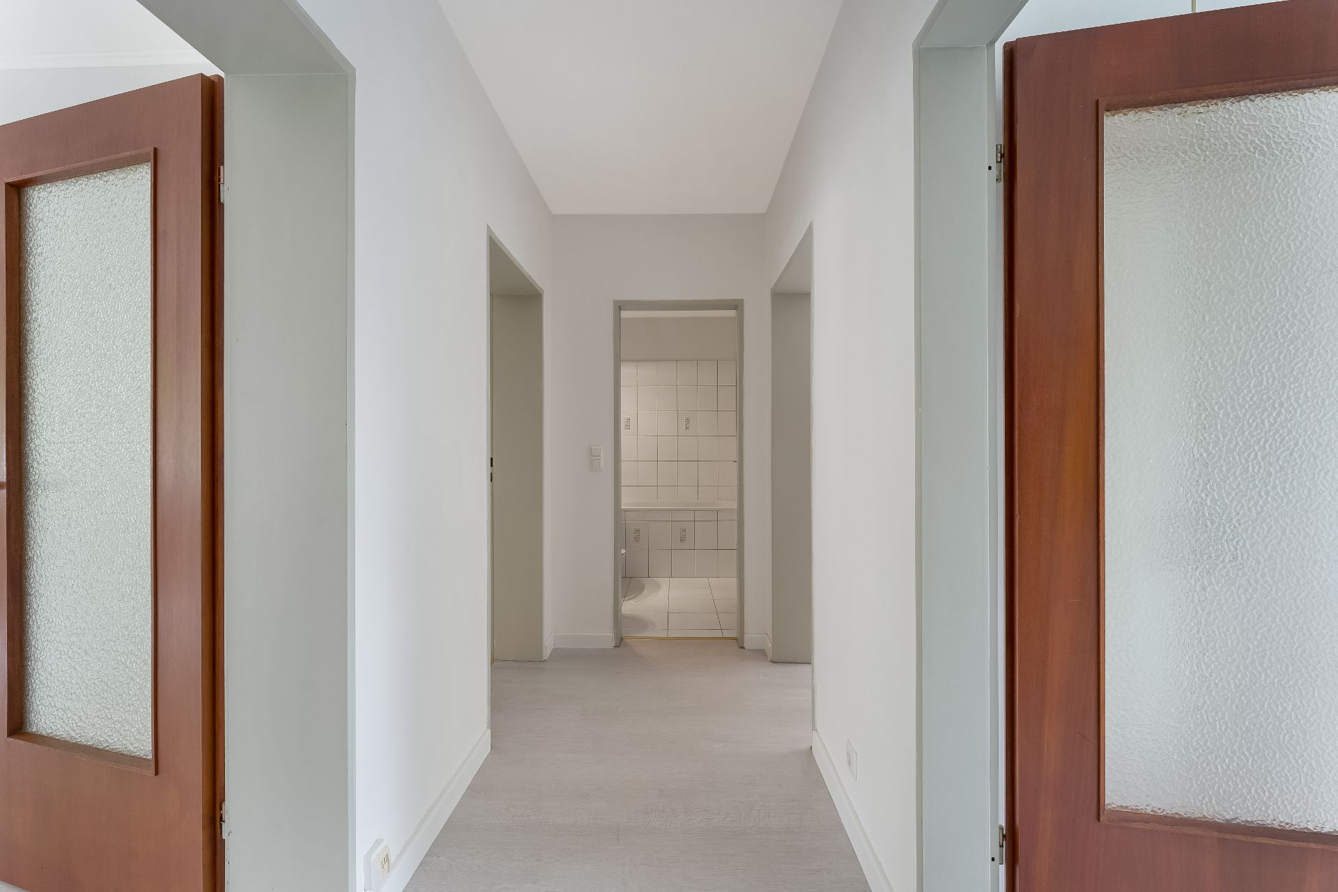Heller Flur mit weißen Wänden, Türen mit Milchglas und Blick ins geflieste Badezimmer.