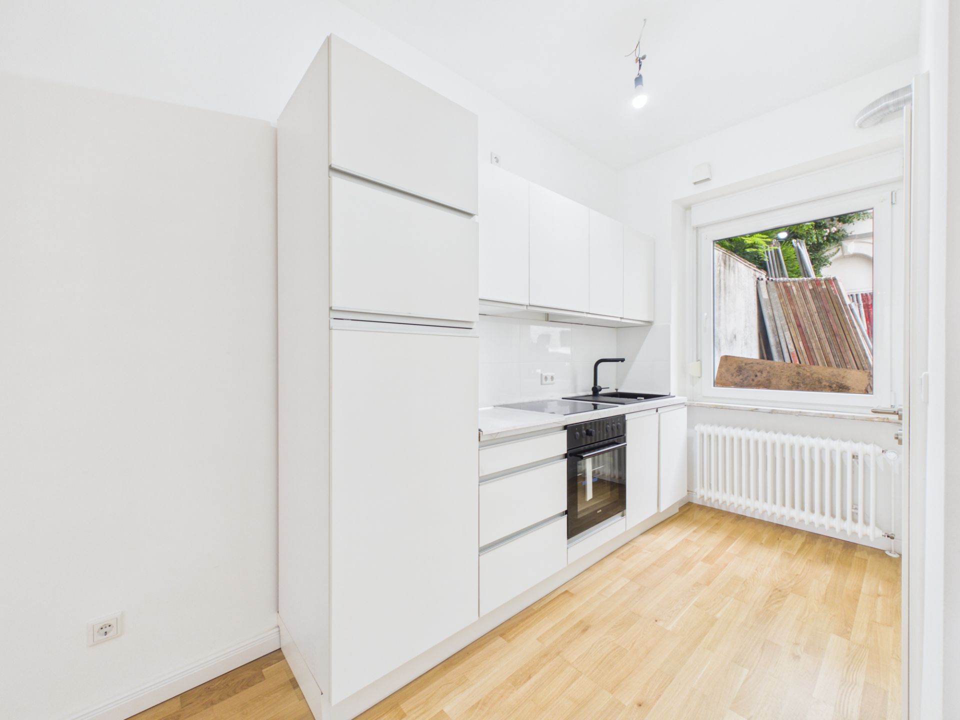 Helle, schmale Einbauküche mit weißen Schränken, Holzfußboden und großem Fenster.