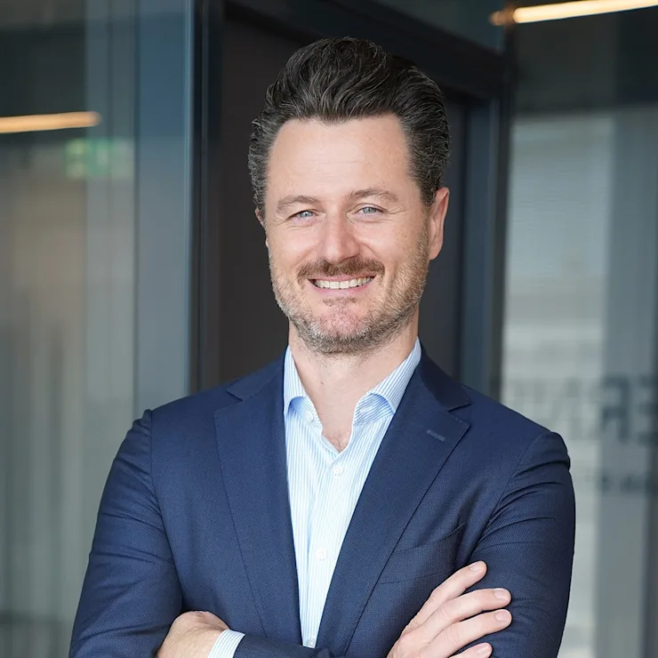 Mann im blauen Anzug steht mit verschränkten Armen in modernem Innenraum.