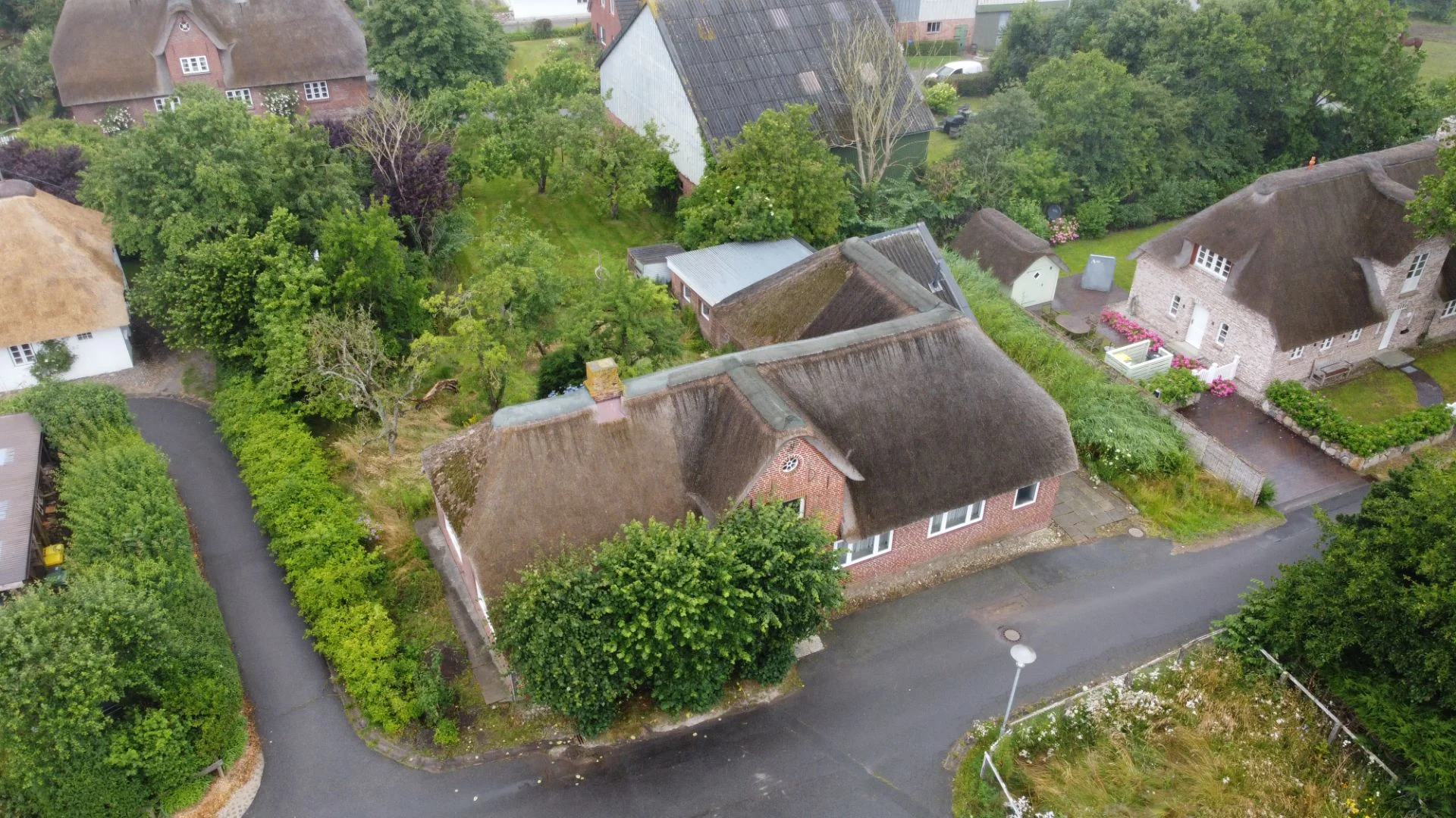 Luftaufnahme eines Hauses mit Reetdach, umgeben von Bäumen und Straßen.