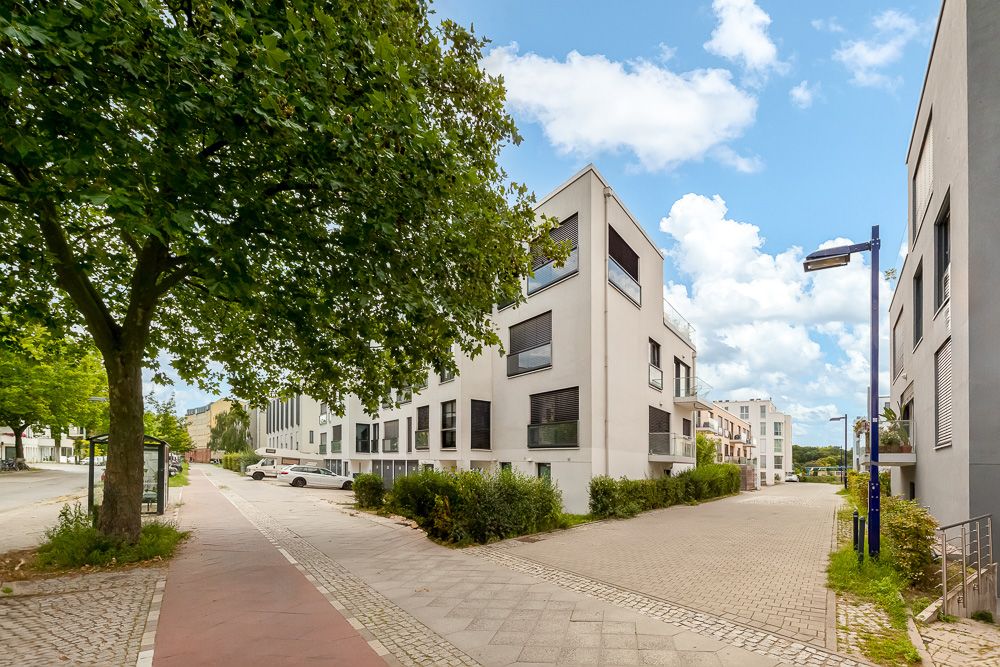 Moderne Wohngebäude an einer ruhigen Straße mit Gehweg und Bäumen.