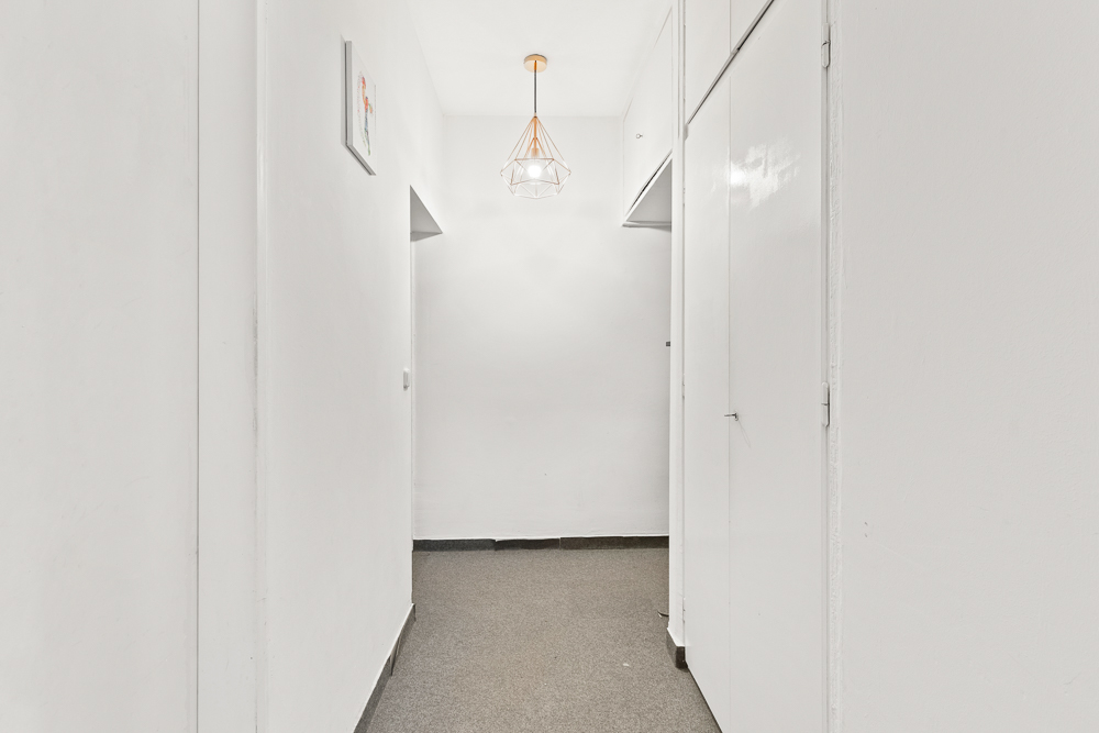Heller Flur mit weiß gestrichenen Wänden, grauem Boden und einer modernen Deckenleuchte.