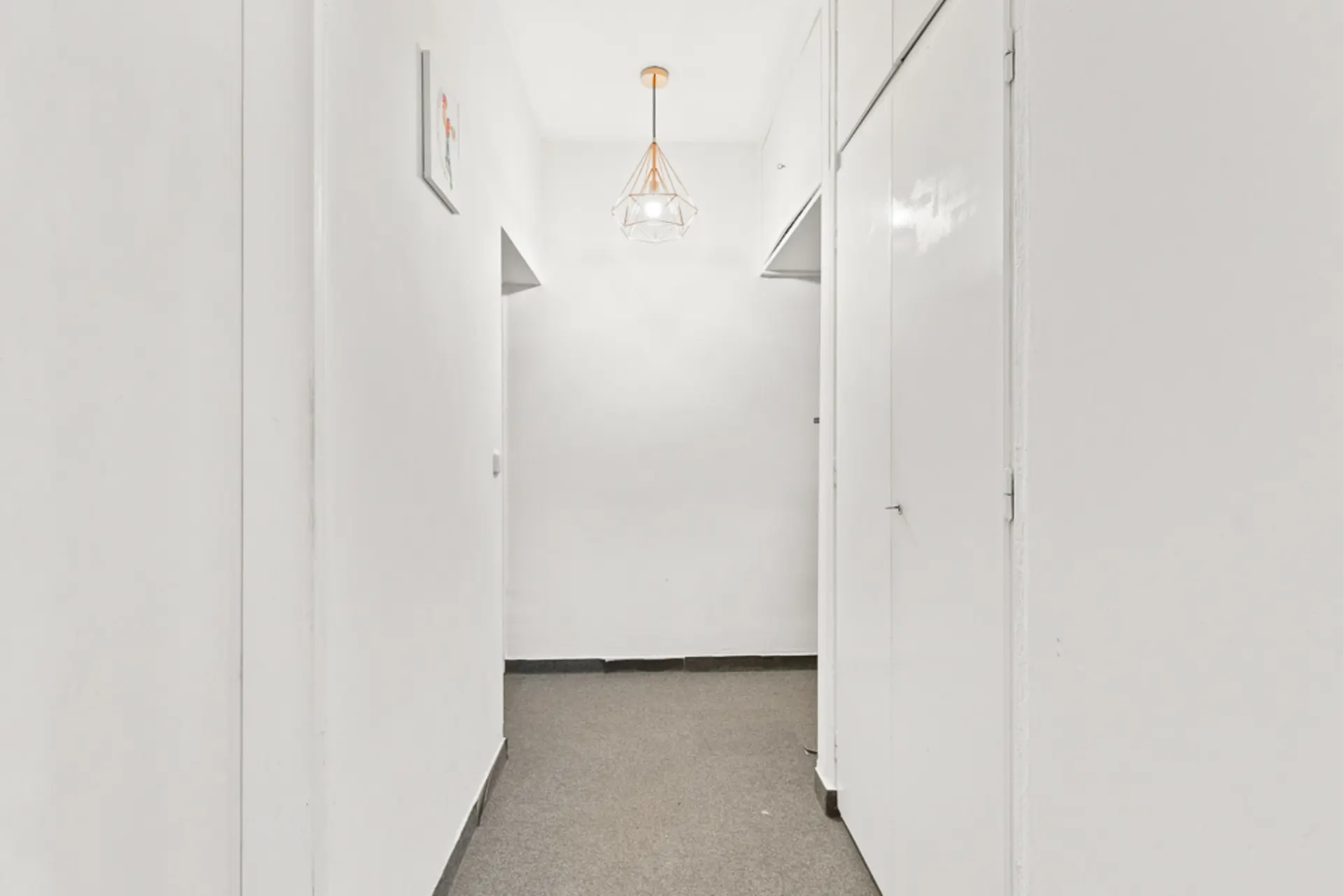 Heller Flur mit weiß gestrichenen Wänden, grauem Boden und einer modernen Deckenleuchte.