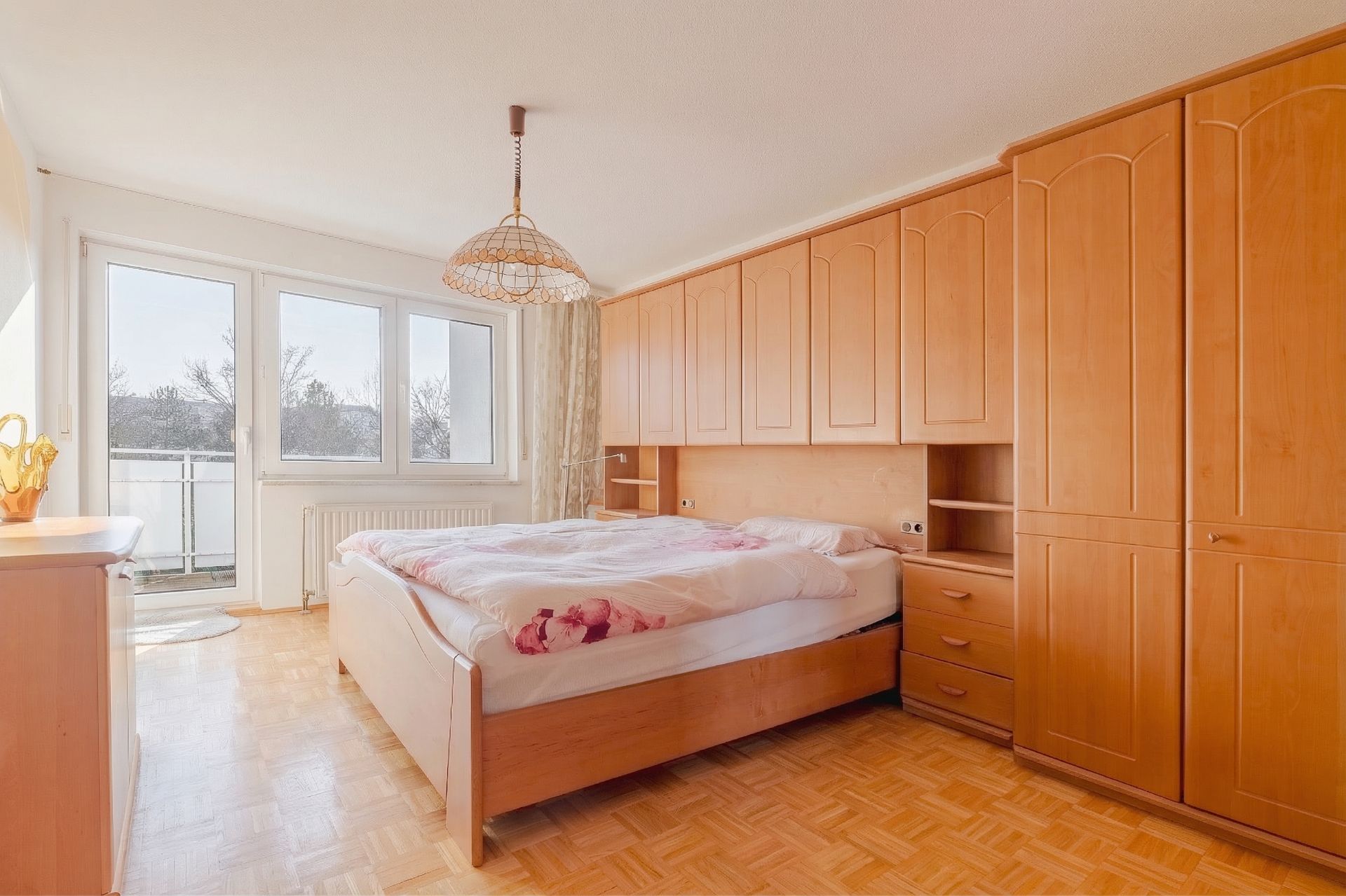 Helles Schlafzimmer mit großem Bett, Einbauschränken aus Holz und Zugang zum Balkon.