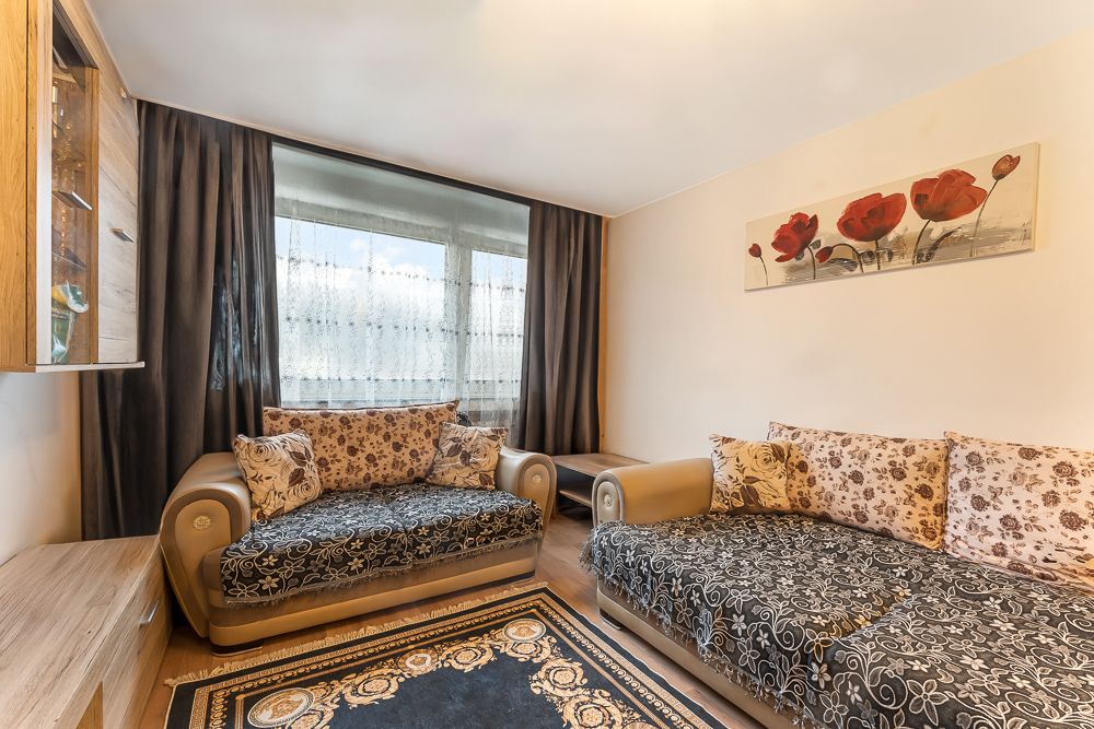 Wohnzimmer mit zwei Sofas, Teppich, großem Fenster, dunklen Vorhängen und Blumenbild an der Wand.