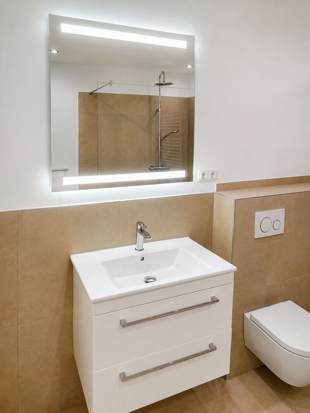 Modernes Badezimmer mit beleuchtetem Spiegel, Waschbecken, Hängeschrank und Wandtoilette.